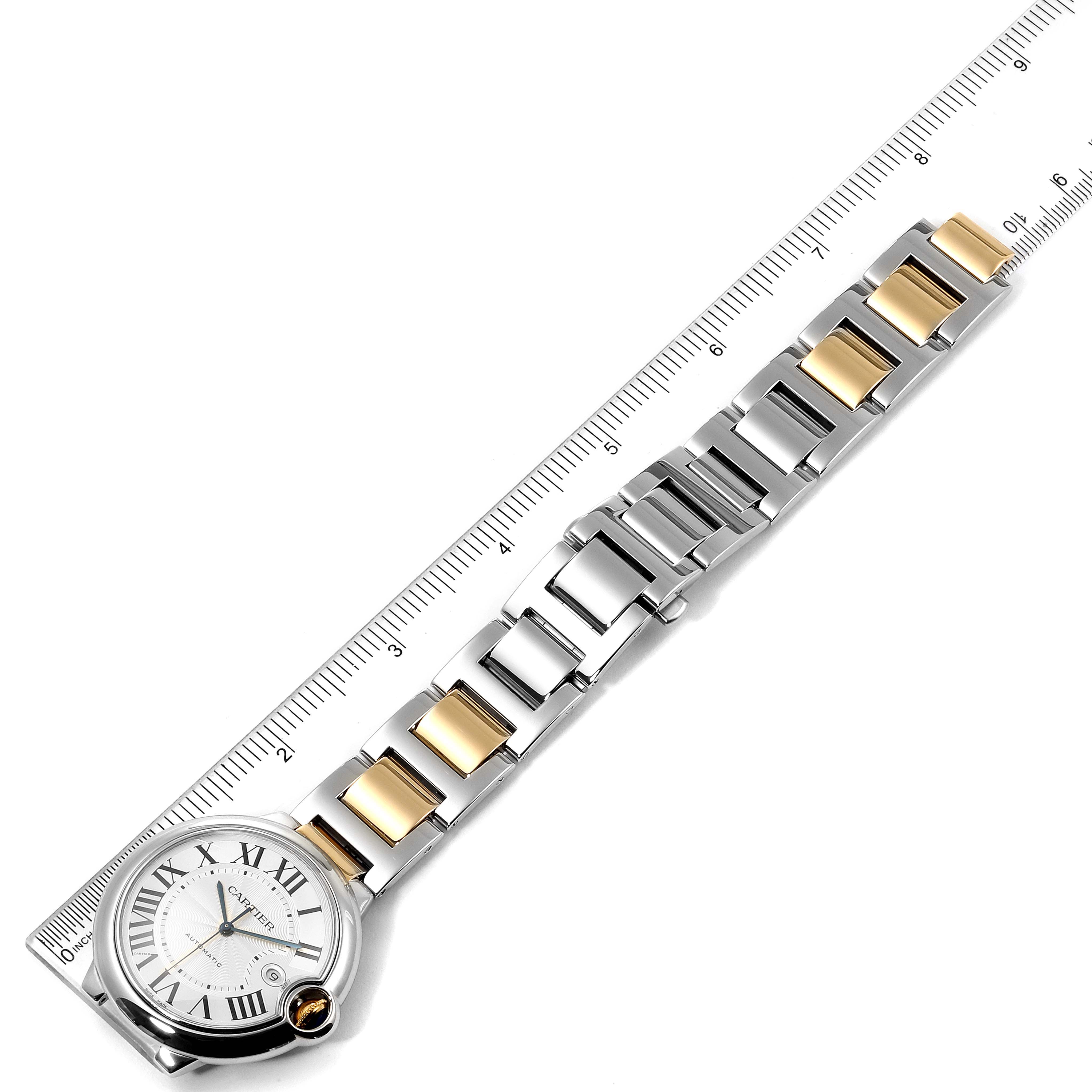 The image shows a Ballon Bleu model by Cartier wristwatch, laid flat with the face and metal bracelet visible alongside a ruler.