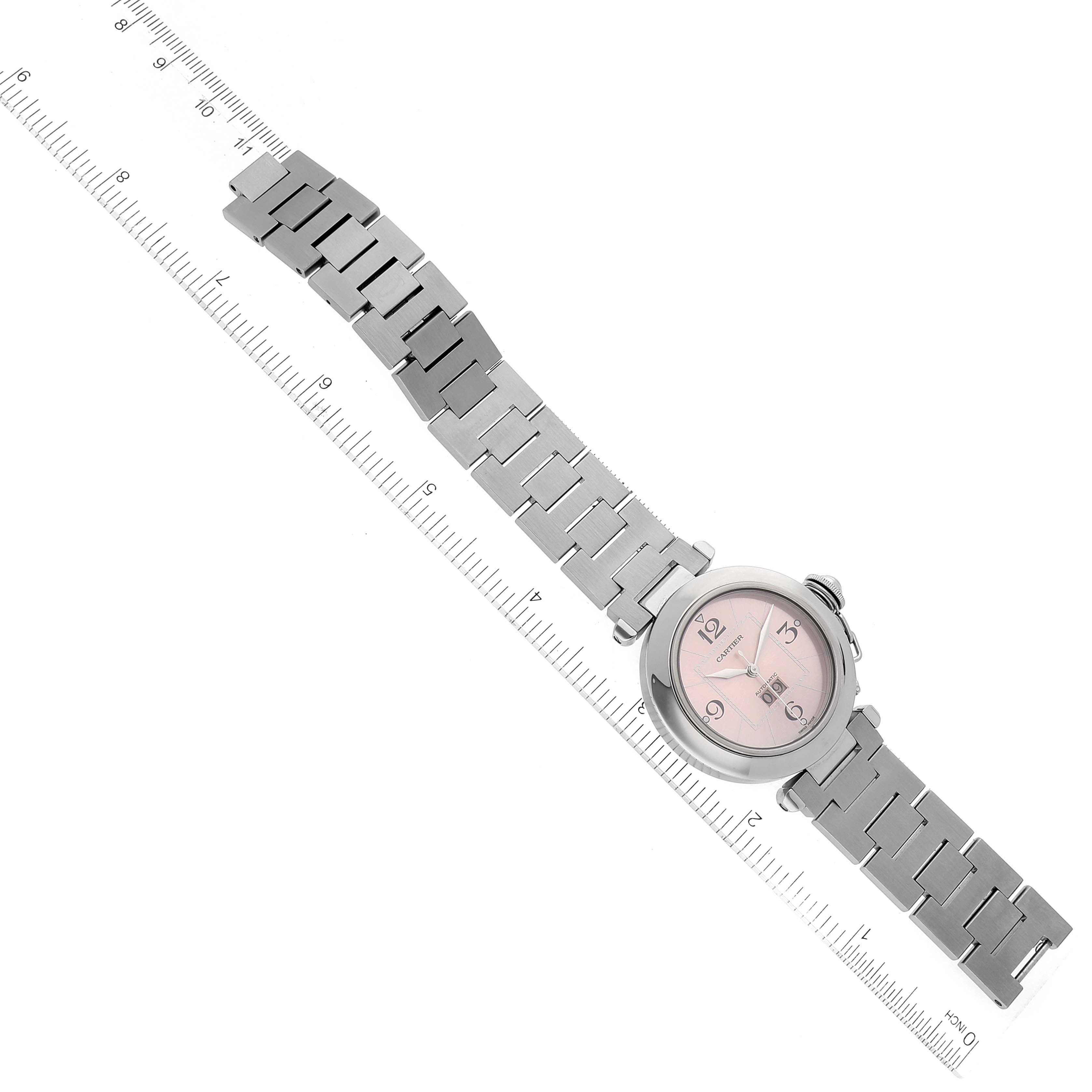 The image shows a Cartier Pasha W31058M7 Women's Stainless Steel Pink Dial W31058M7 Women's Stainless Steel Pink Dial watch laid flat with a ruler, highlighting its bracelet, dial, and case from an overhead angle.