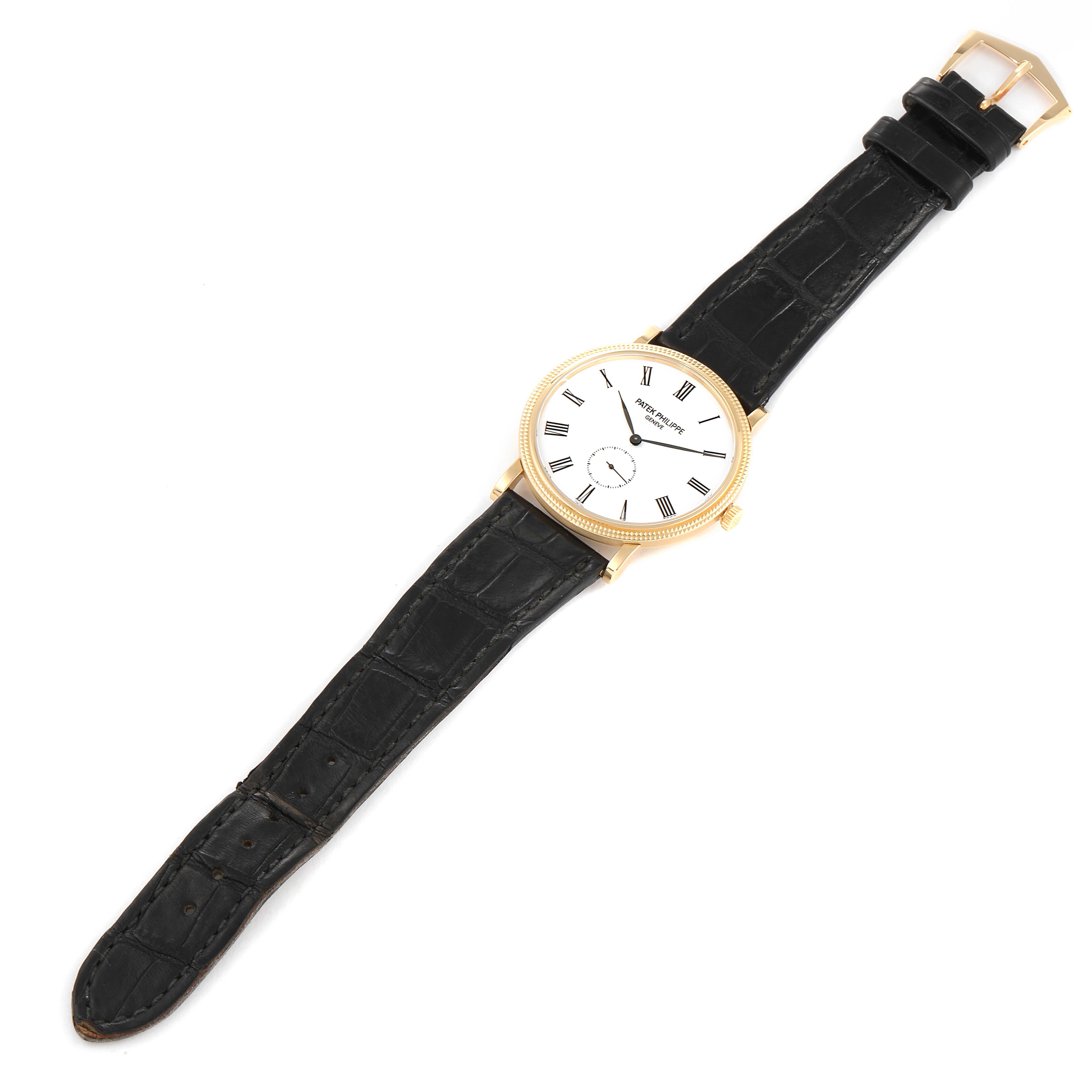 The image shows a top-down view of a Patek Philippe Calatrava 5119J-001 Men's Yellow Gold White Dial 5119J-001 Men's Yellow Gold White Dial watch, featuring its round dial, black leather strap, and gold casing.