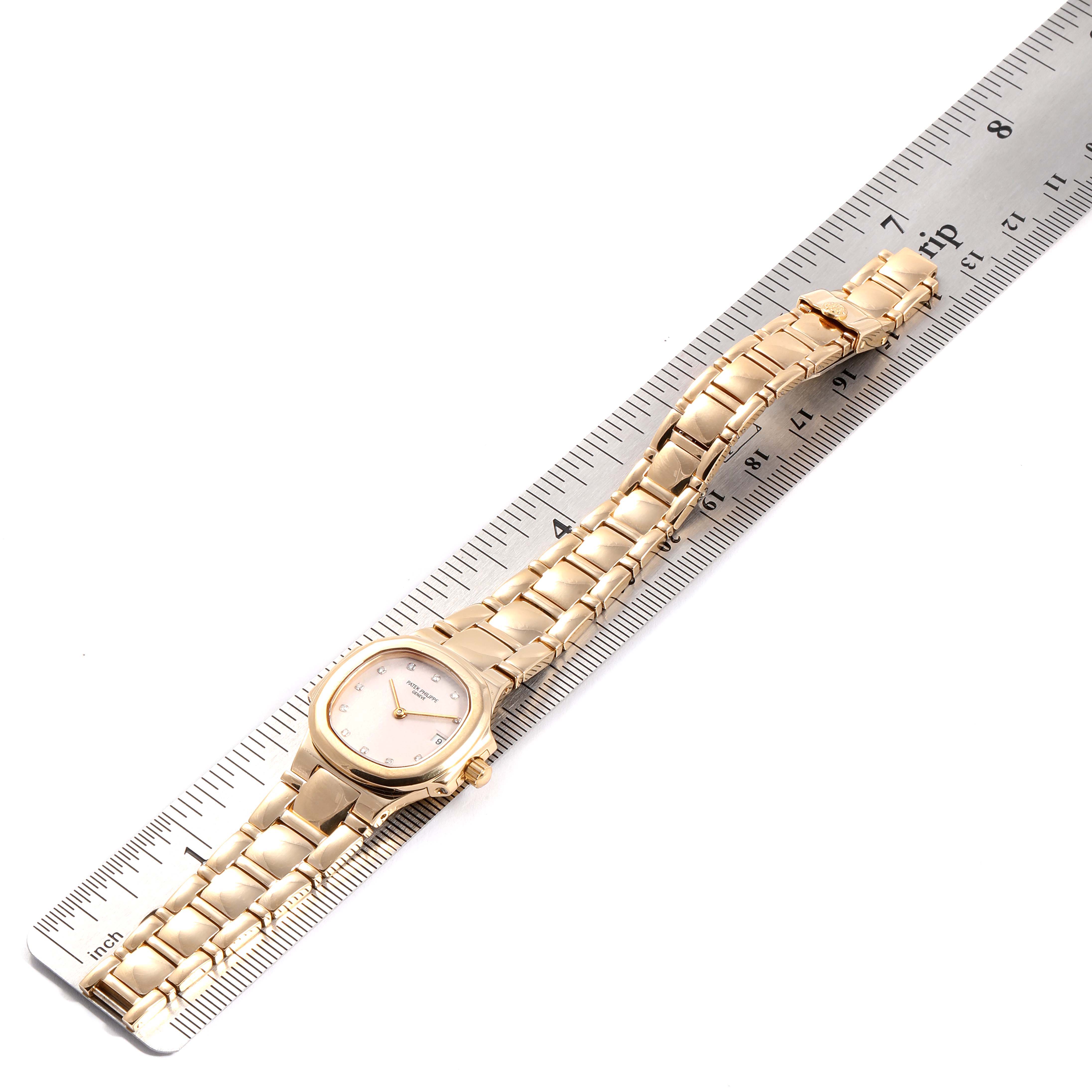 The image shows a Patek Philippe Nautilus 4700 Women's Yellow Gold Beige Dial 4700 Women's Yellow Gold Beige Dial watch laid flat on a ruler, displaying its face, bracelet, and clasp.
