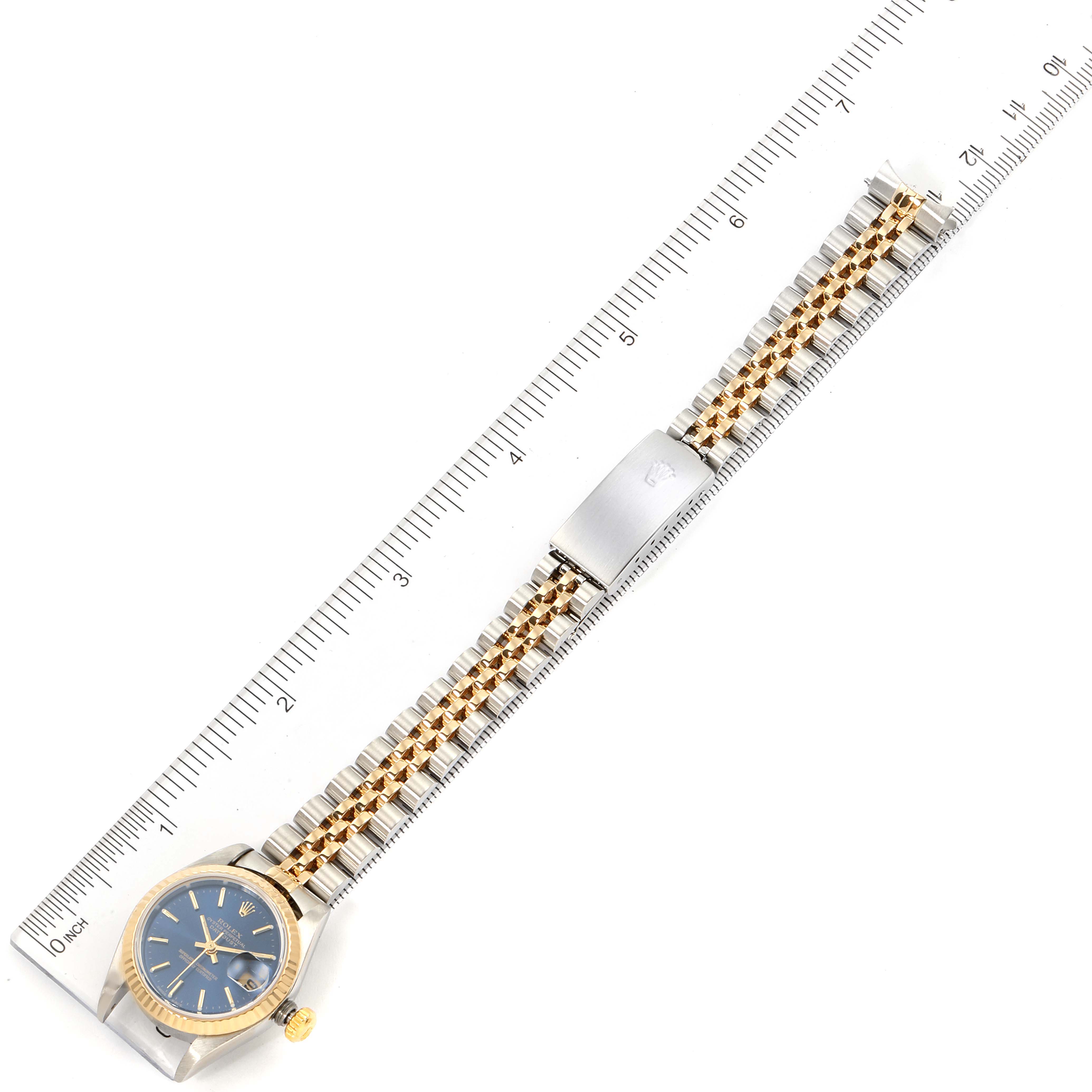 The Rolex Datejust 79173 Women's Steel and Gold (two tone) Blue Dial 79173 Women's Steel and Gold (two tone) Blue Dial watch is shown from a top-down angle, highlighting the face, bracelet, and clasp next to a ruler.