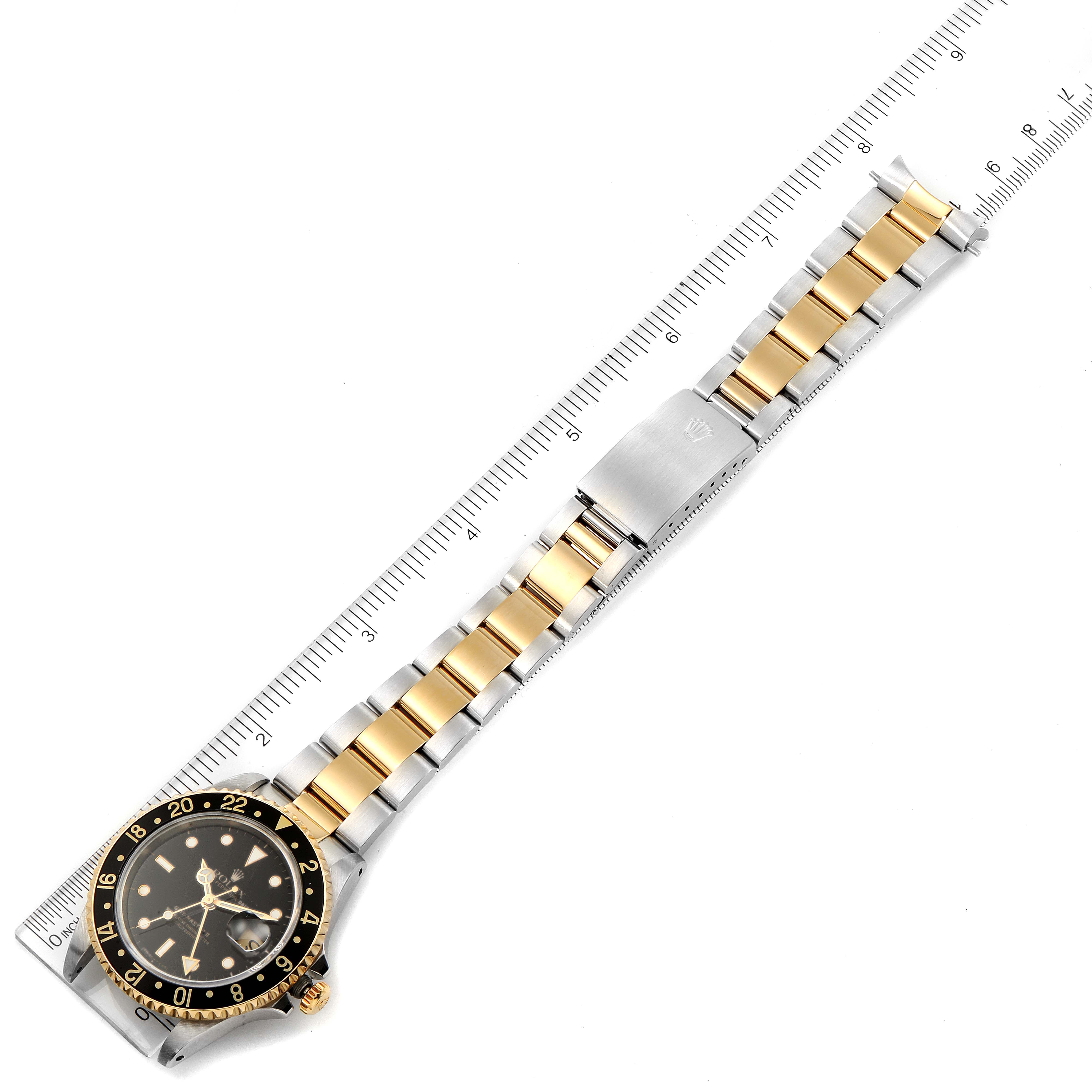 The image shows a Rolex GMT-Master 16713 Men's Steel and Gold (two tone) Black Dial 16713 Men's Steel and Gold (two tone) Black Dial watch laid flat with its bracelet and bezel visible, alongside a measurement ruler.