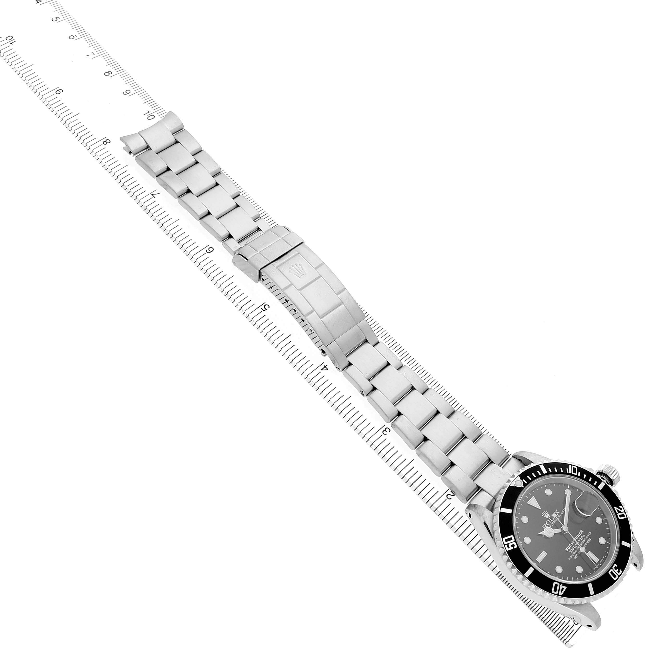 The Rolex Submariner 16610 Men's Stainless Steel Black Dial watch is shown in a top-down angle, featuring the face, bezel, and metal bracelet alongside a ruler for scale.