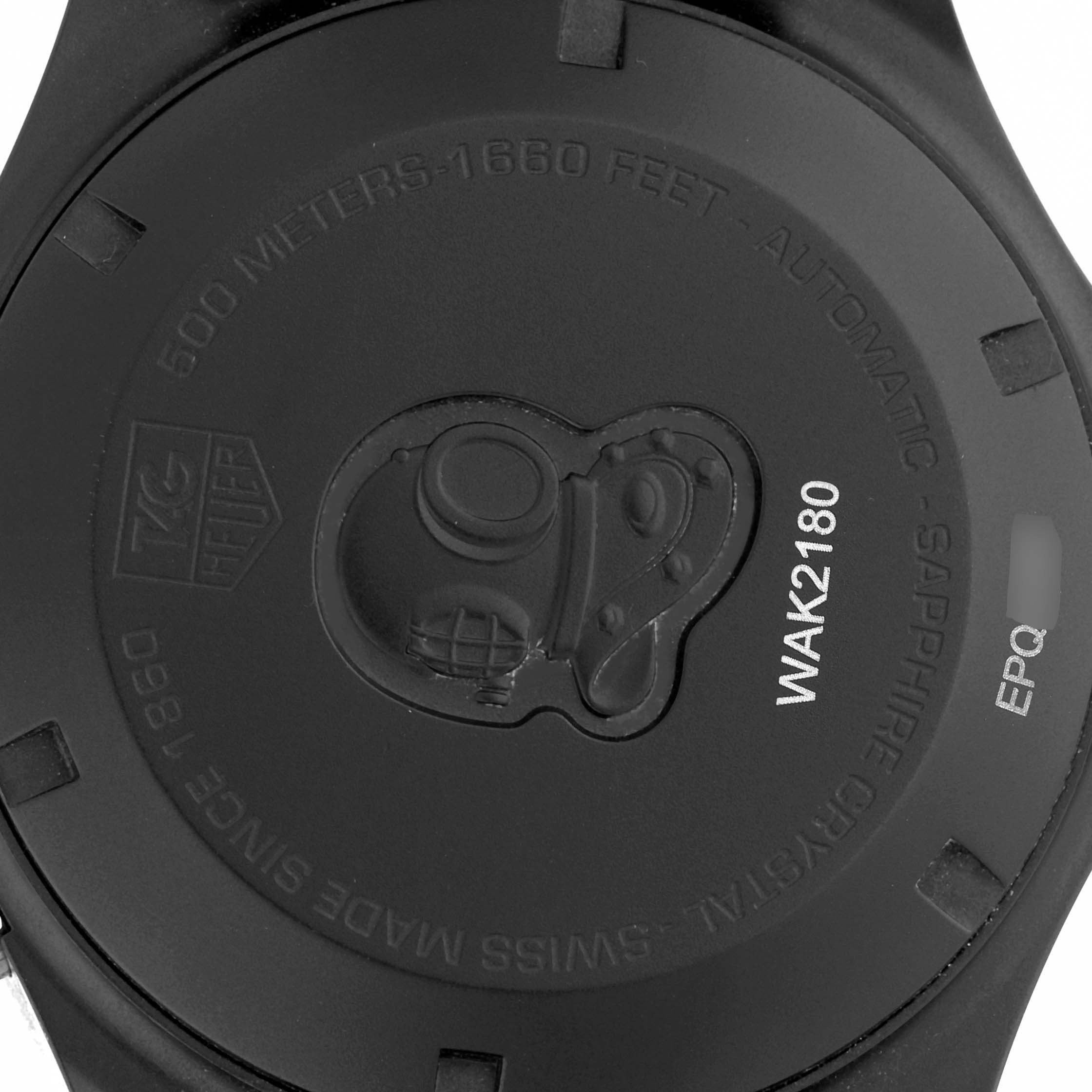 The image shows the back of a Tag Heuer Aquaracer WAK2180.FT6027 Men's Titanium Black Dial watch, featuring engravings, including a helmet design and text details.