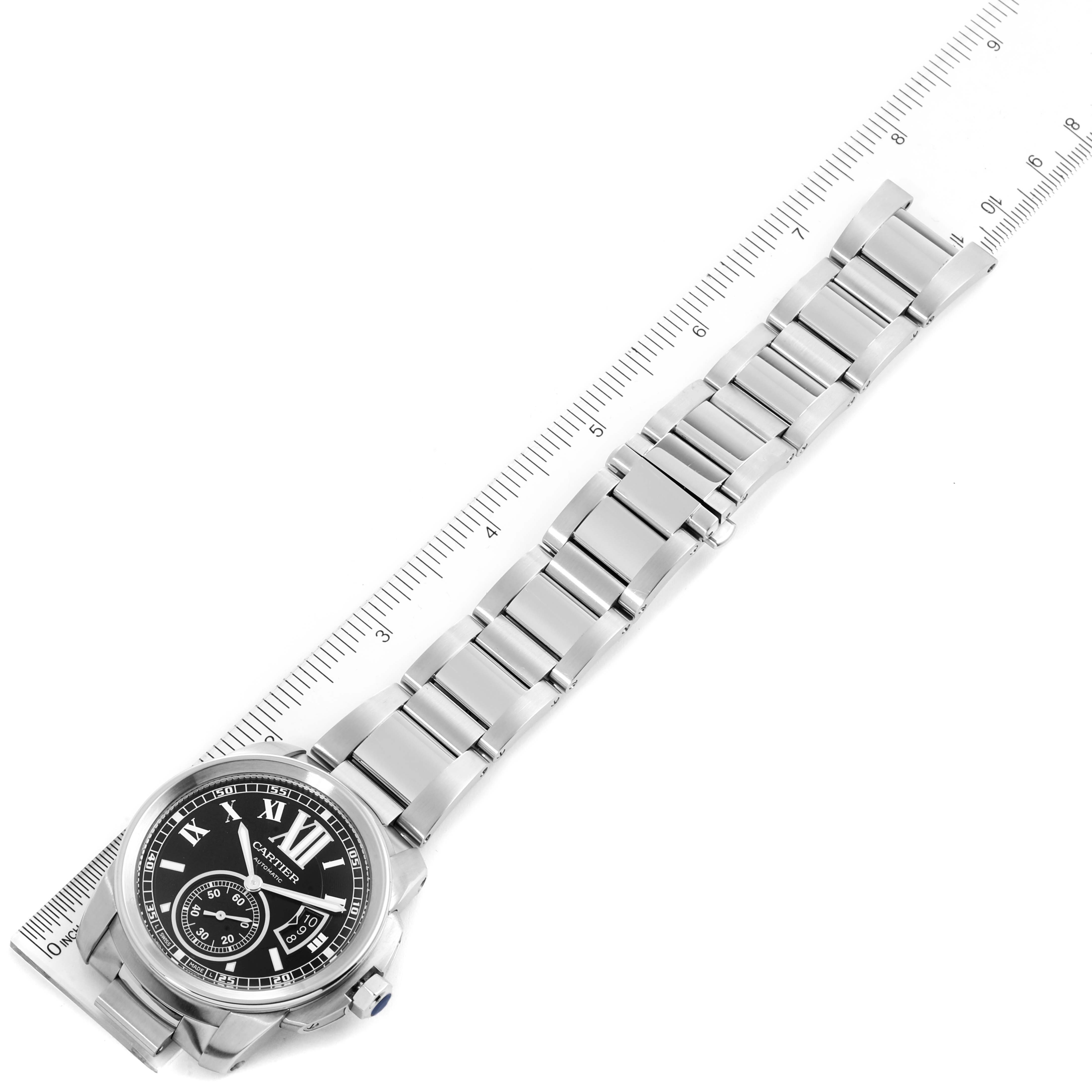This image shows a top view of a Calibre de Cartier watch by Cartier, highlighting the watch face and entire metal bracelet alongside a measuring ruler.