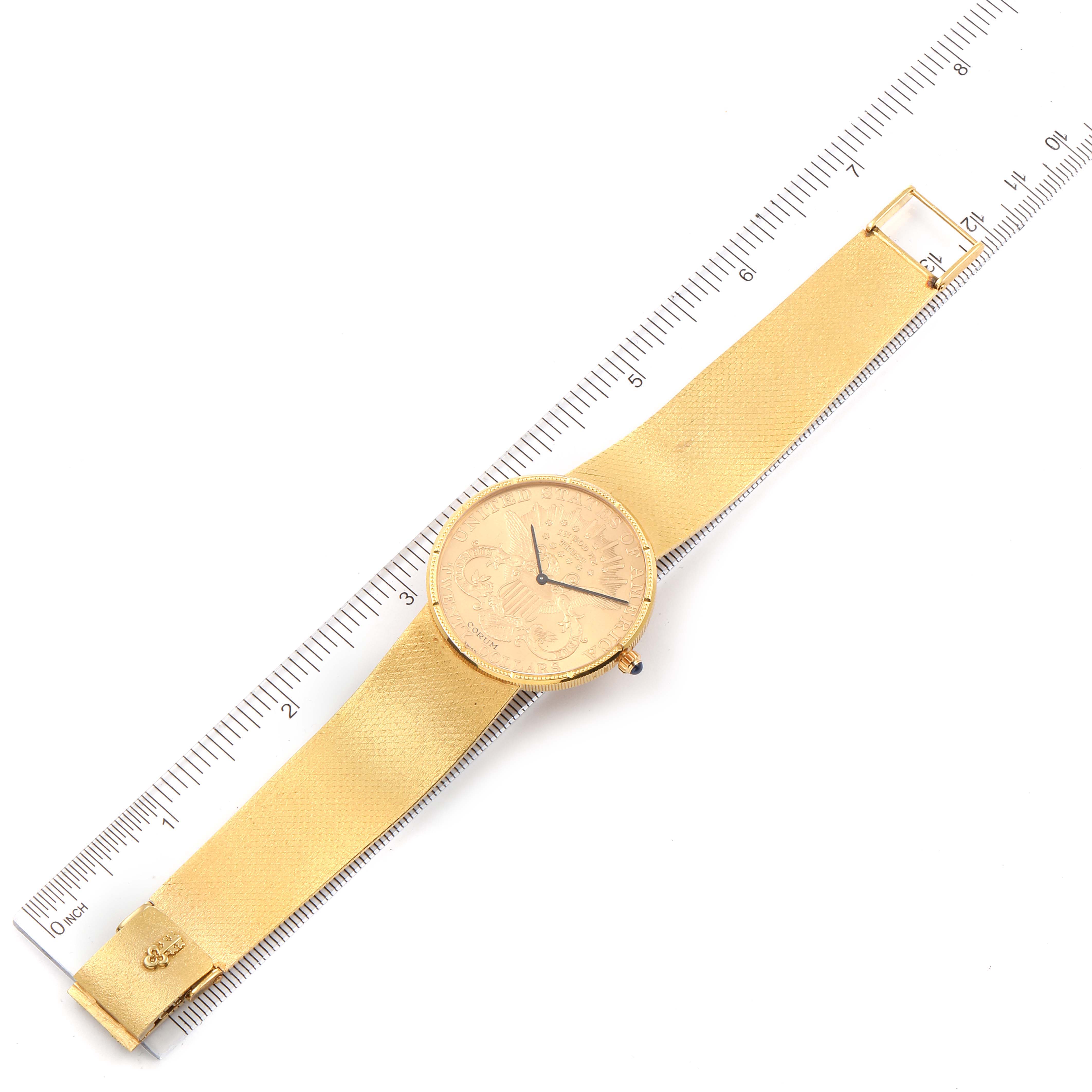 The image shows a top view of a Corum Coin Watch 1897 Men's Yellow Gold Black Dial 1897 Men's Yellow Gold Black Dial model with its strap fully extended next to a ruler.