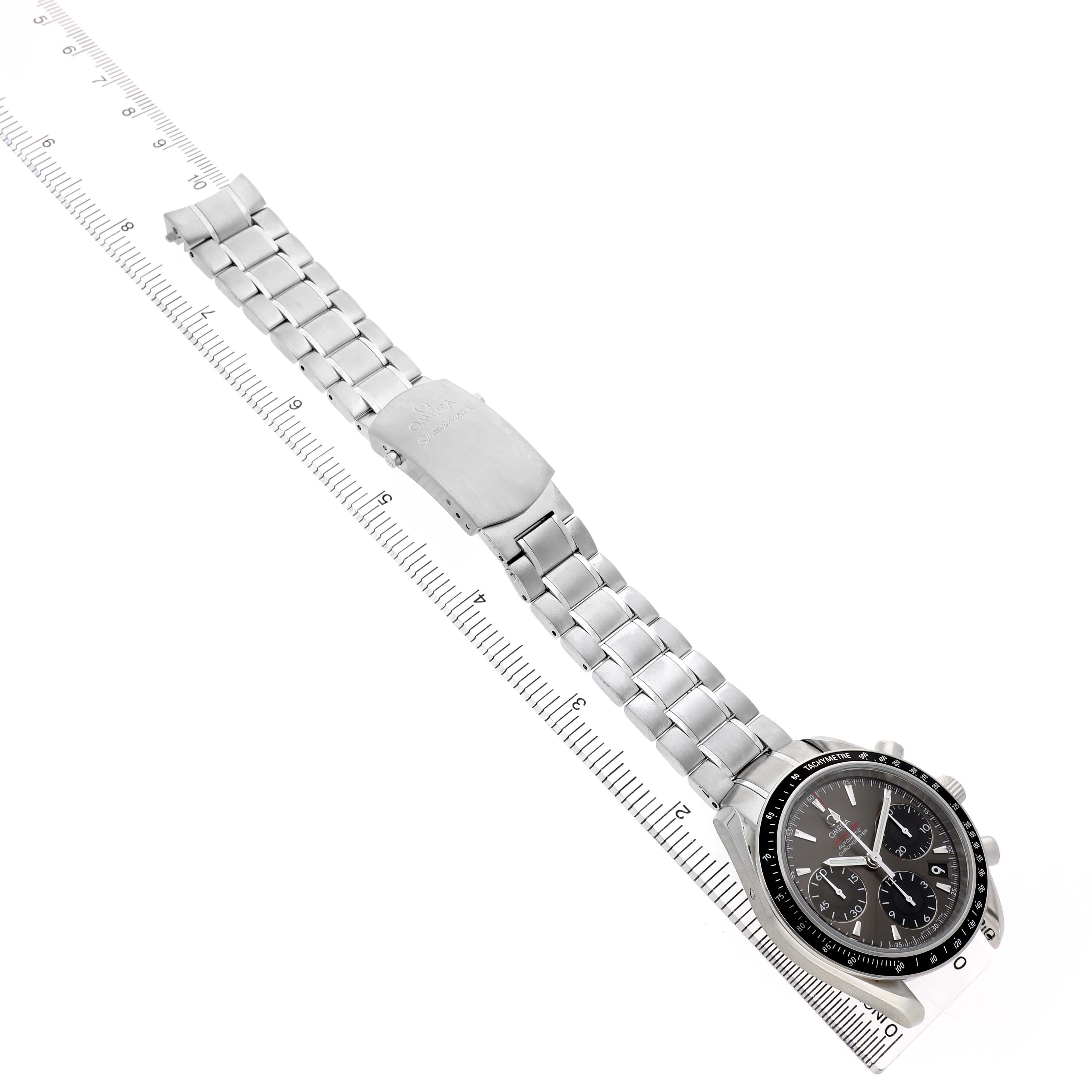 The Omega Speedmaster 323.30.40.40.06.001 Men's Stainless Steel Grey Dial watch is shown at an oblique angle, displaying the face, bezel, bracelet, and clasp fully extended next to a ruler.
