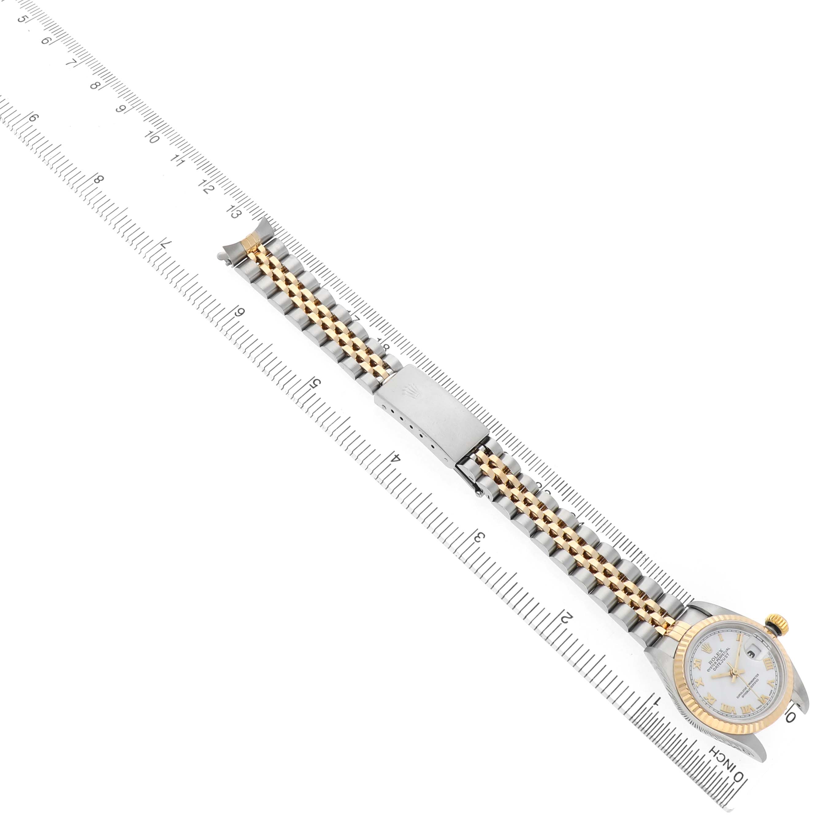 The Rolex Datejust 79173 Women's Steel and Gold (two tone) White Dial watch is shown from the top, highlighting the bracelet, clasp, and part of the face next to a ruler.