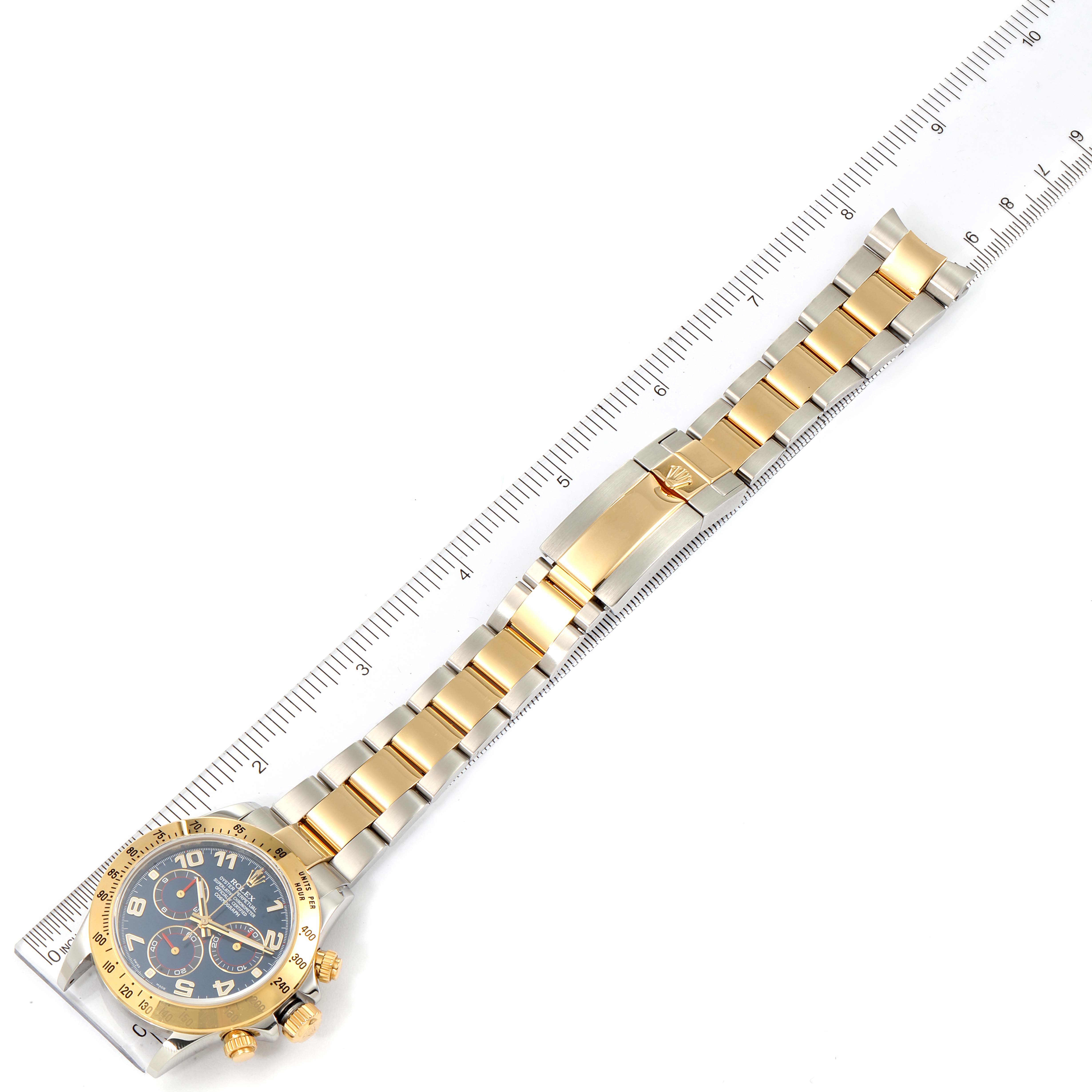 The image shows a Rolex Daytona 116523 Men
s Steel and Gold (two tone) Blue Dial 116523 Men
s Steel and Gold (two tone) Blue Dial watch laid flat with the bracelet extended along a ruler.