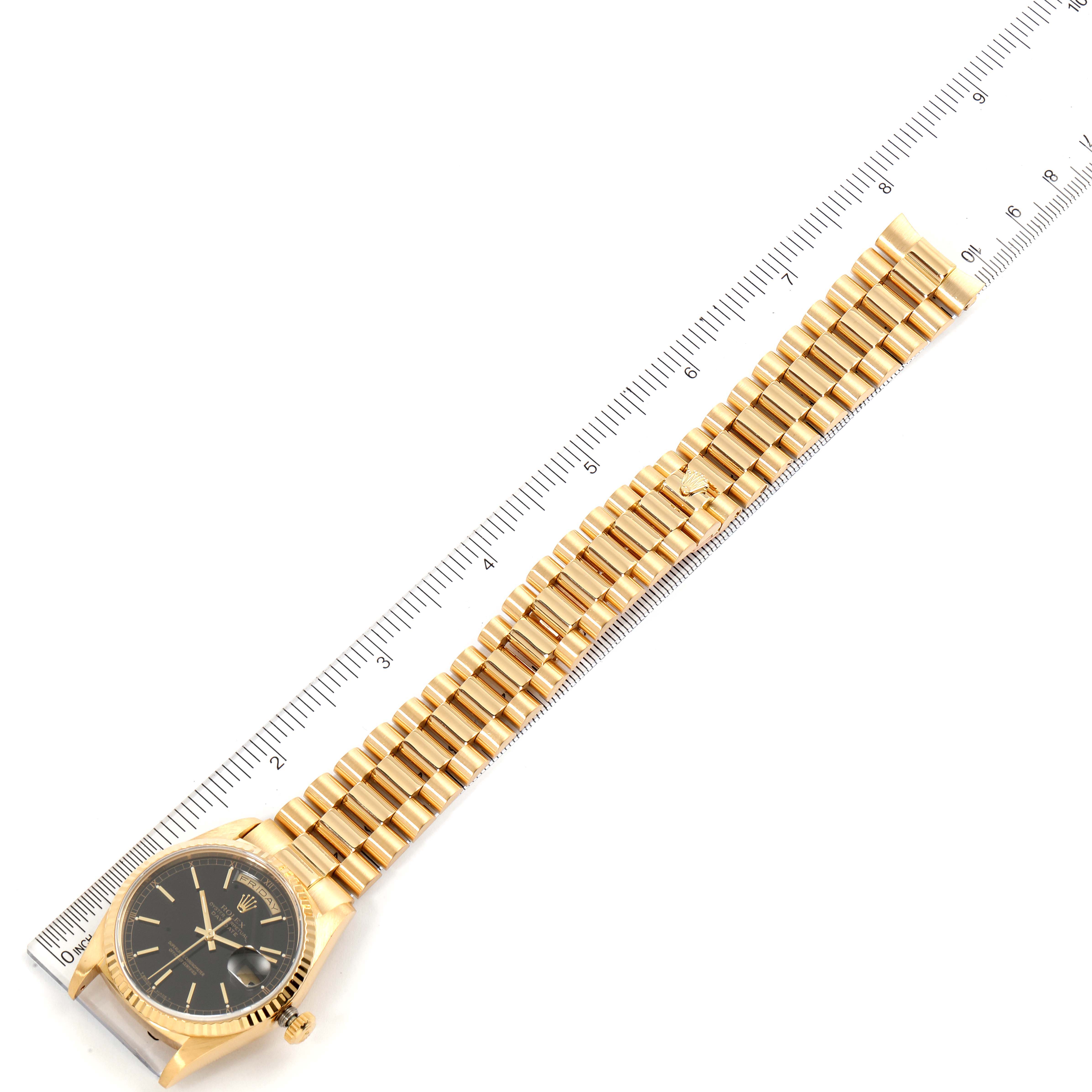 The image shows a Rolex President 18238 Men
s Yellow Gold Black Dial 18238 Men
s Yellow Gold Black Dial model watch laid flat against a ruler, highlighting its gold bracelet and black dial.