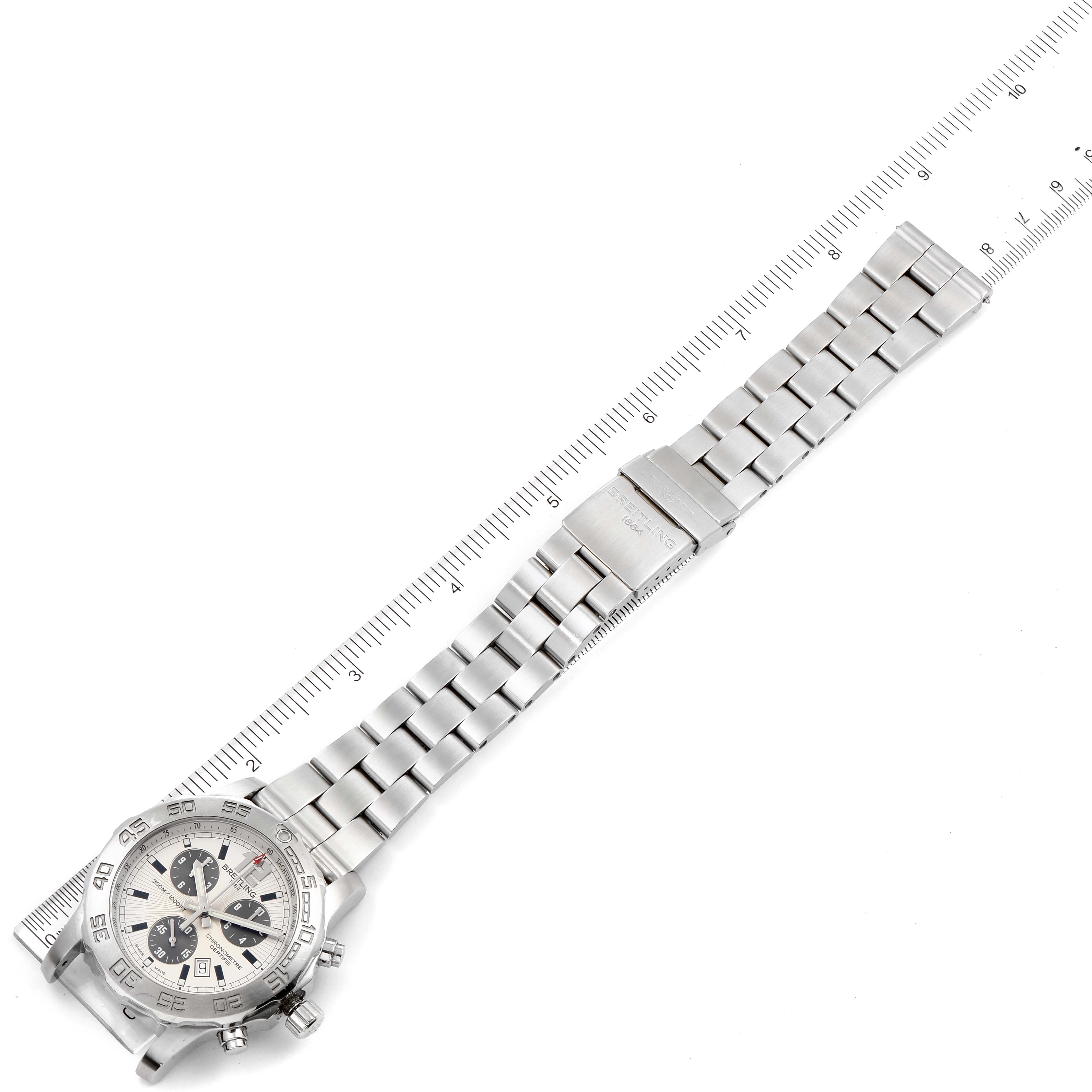 The image shows a Breitling Colt A73387 Men
s Stainless Steel White Dial A73387 Men
s Stainless Steel White Dial watch lying flat, showcasing its face and metal bracelet with a ruler for scale.
