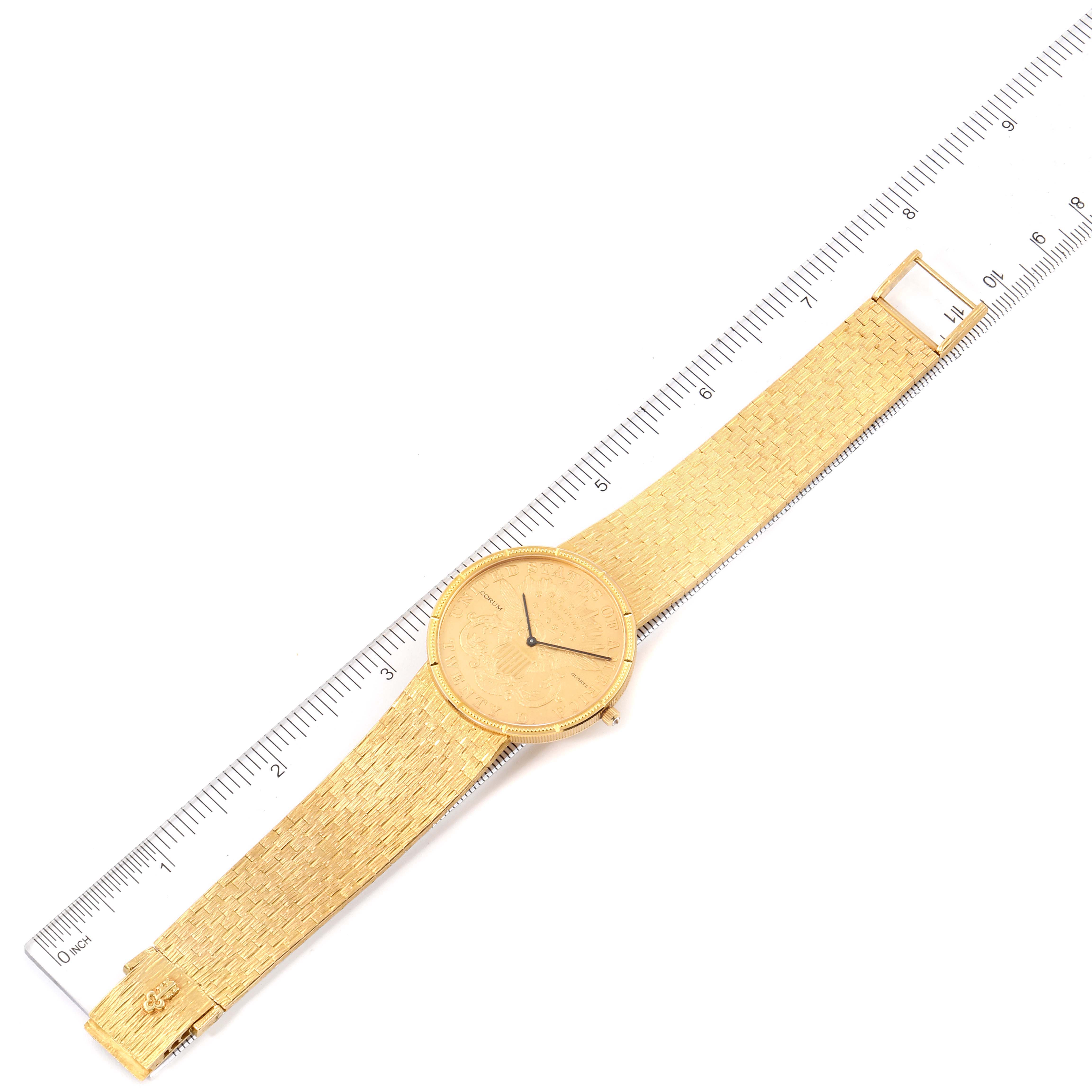 The image shows a top-down view of a Corum Coin Watch 1875  Men's Yellow Gold Black Dial 1875  Men's Yellow Gold Black Dial model, including its face and entire band, with a ruler for scale.