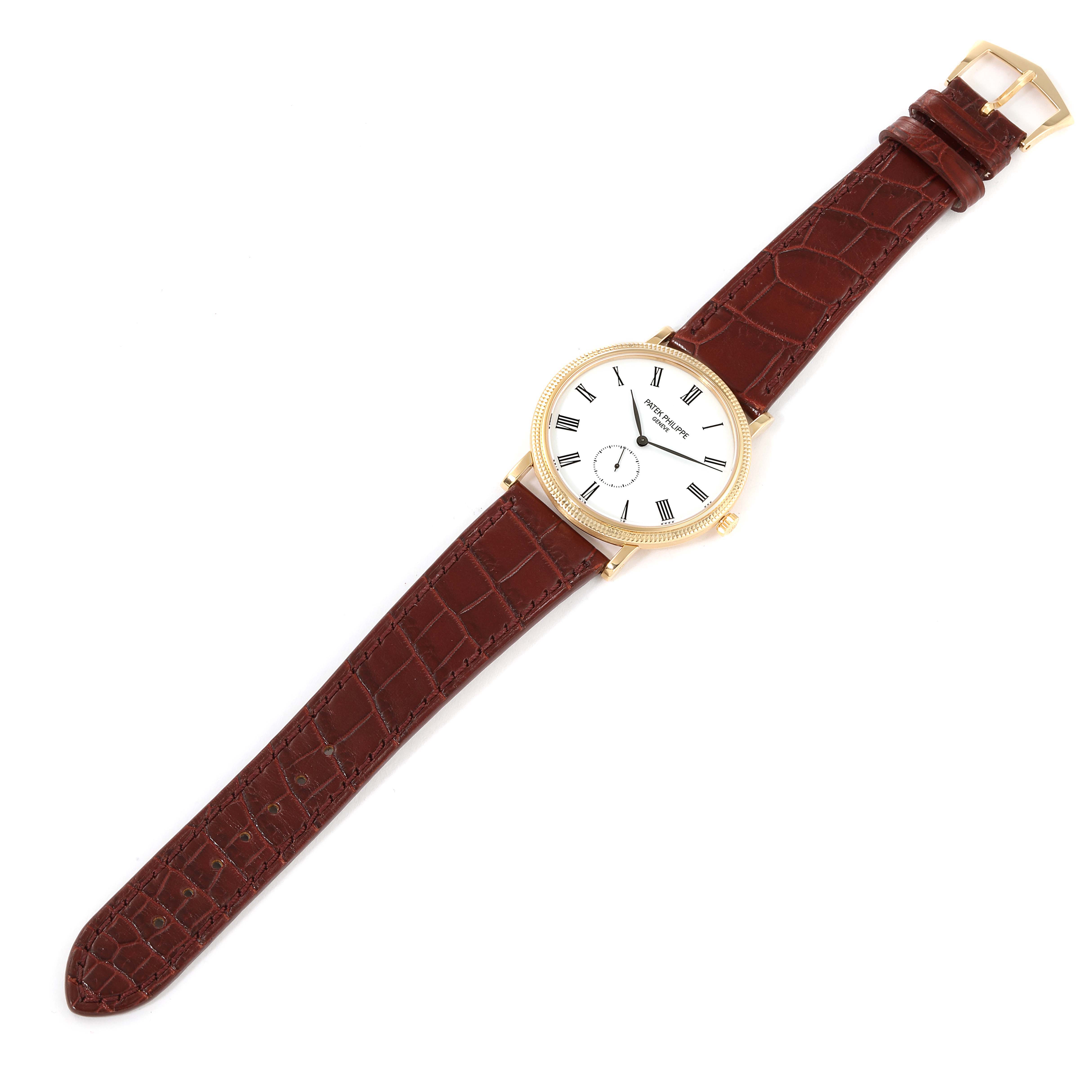 The image shows a Patek Philippe Calatrava 5119J Men's Yellow Gold White Dial 5119J Men's Yellow Gold White Dial watch from a top-down angle, displaying its face, leather strap, and buckle.