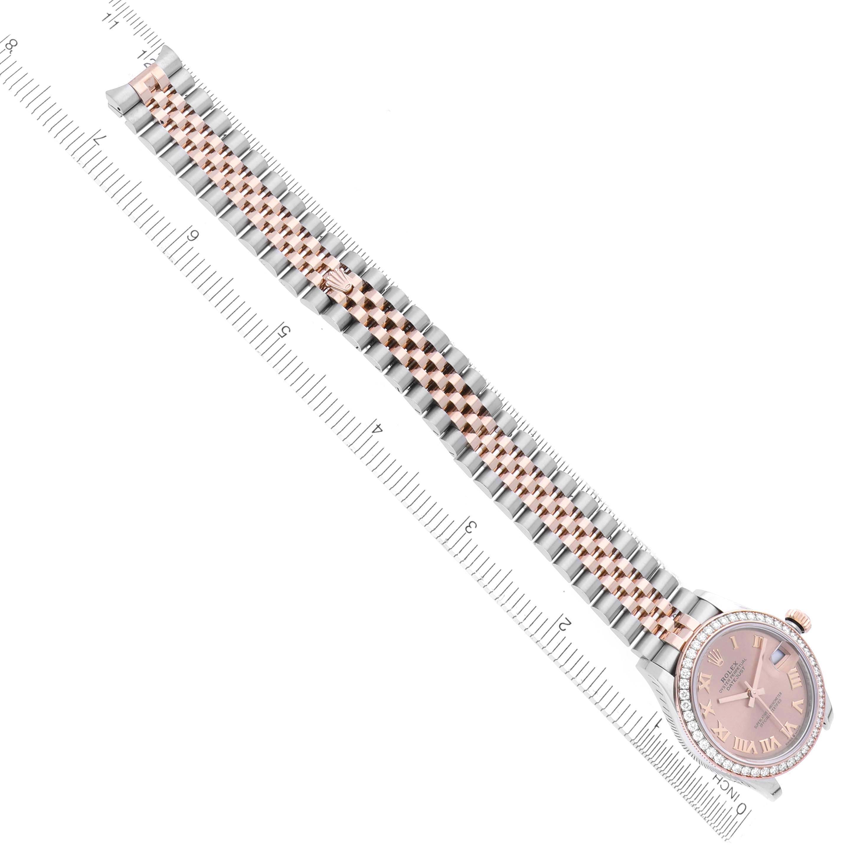 The Rolex Mid-Size 278381 Women's Steel and Gold (two tone) Pink Dial 278381 Women's Steel and Gold (two tone) Pink Dial watch is shown from a top-down angle, highlighting its bracelet and pink dial next to a ruler.