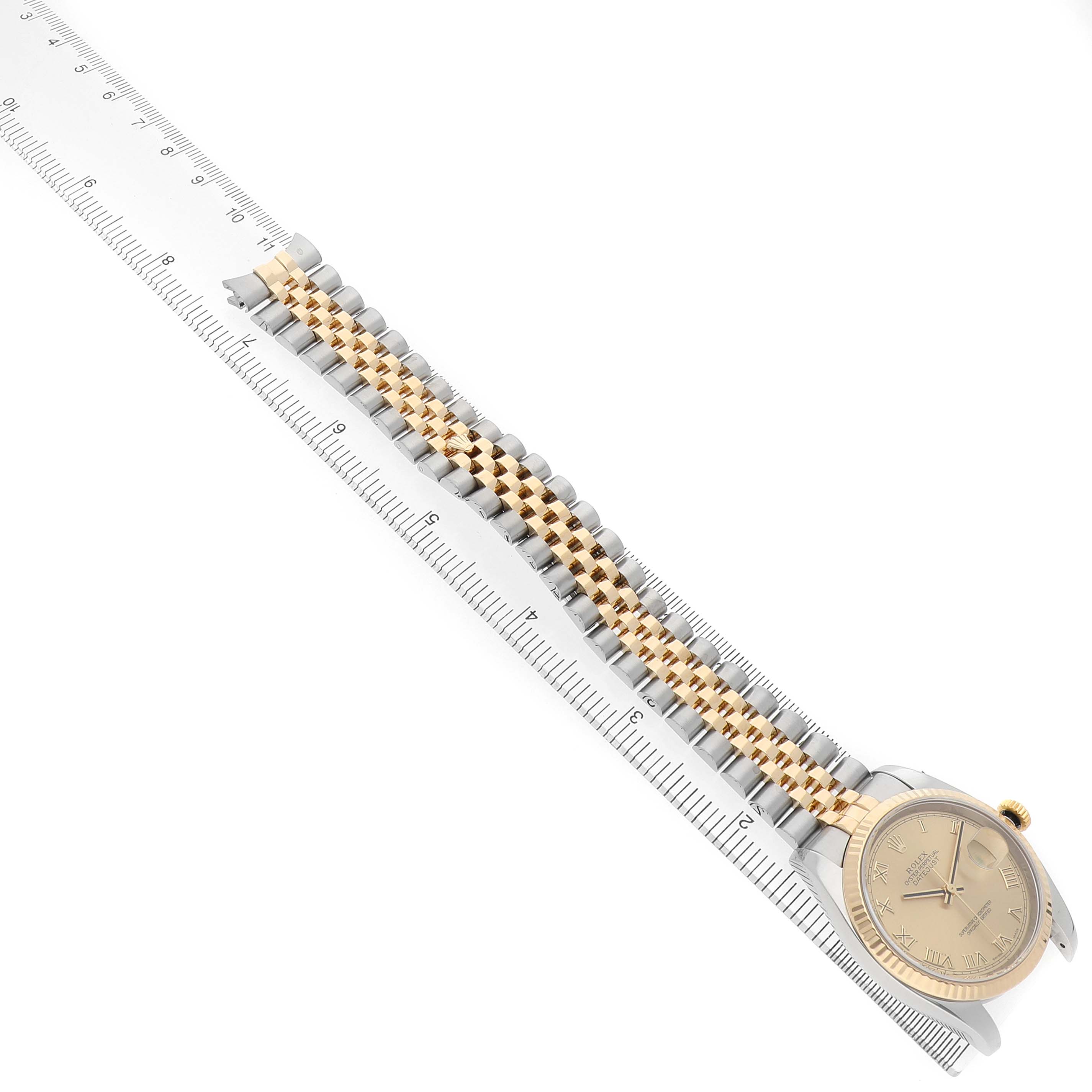 The Rolex Datejust 116233 Women's Steel and Gold (two tone) Champagne Dial watch is shown from a top angle, highlighting the face, bezel, and two-tone bracelet, placed alongside a ruler.
