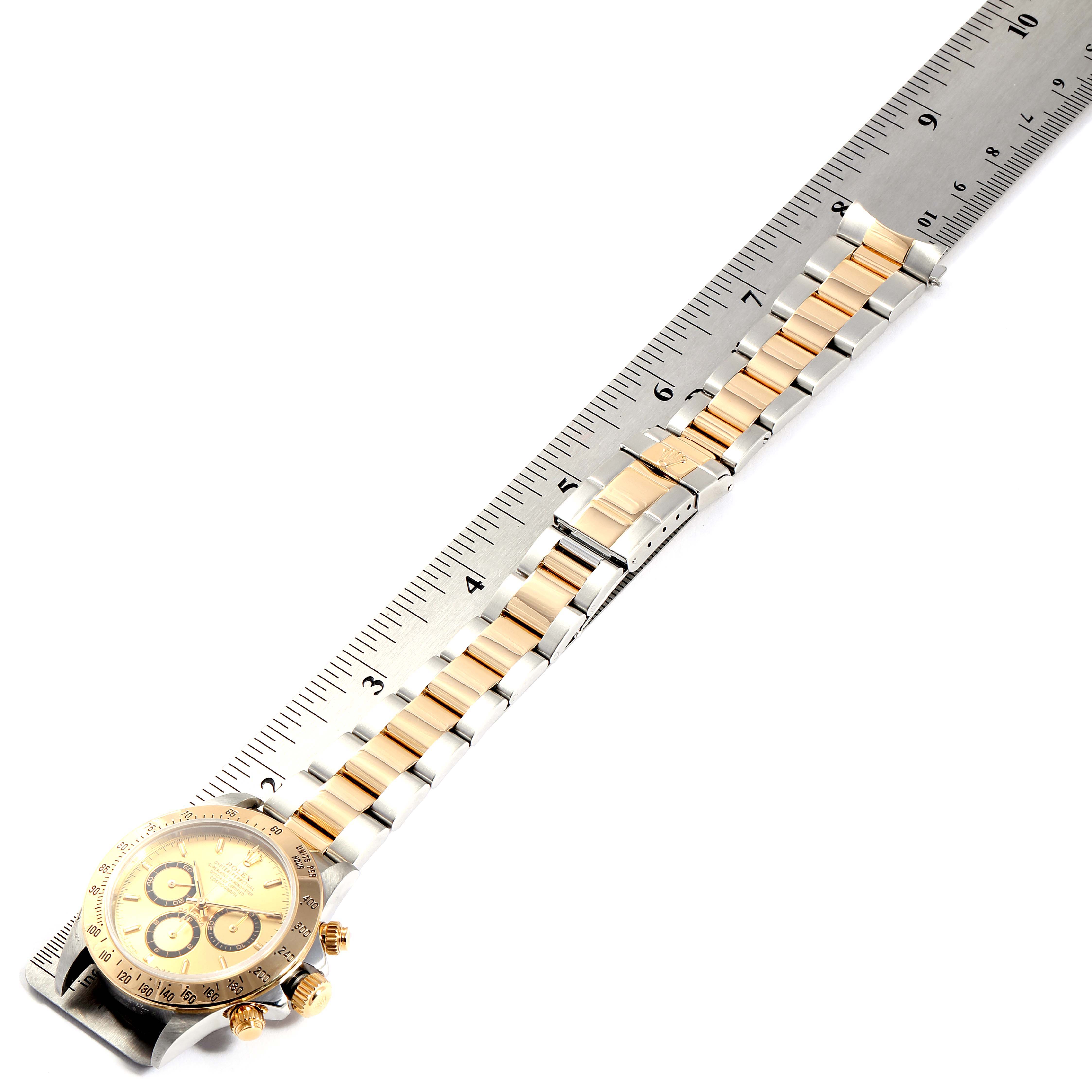 This image shows a Rolex Daytona 16523 Men
s Steel and Gold (two tone) Champagne Dial 16523 Men
s Steel and Gold (two tone) Champagne Dial watch laid flat with its full bracelet and a ruler for measurement.