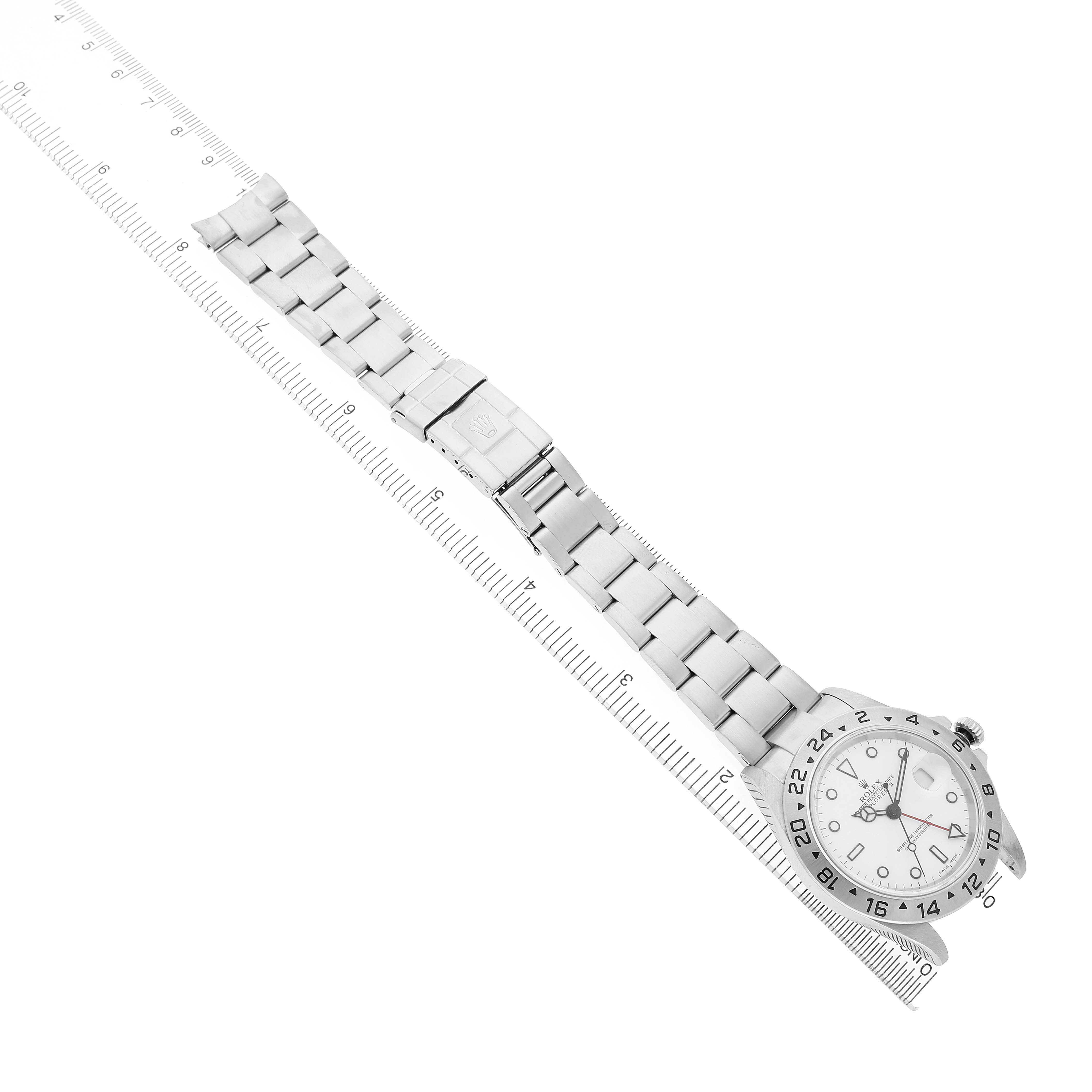 The Rolex Explorer 16570 Men's Stainless Steel White Dial watch is shown from an overhead angle, displaying the bracelet, clasp, and dial beside a ruler.