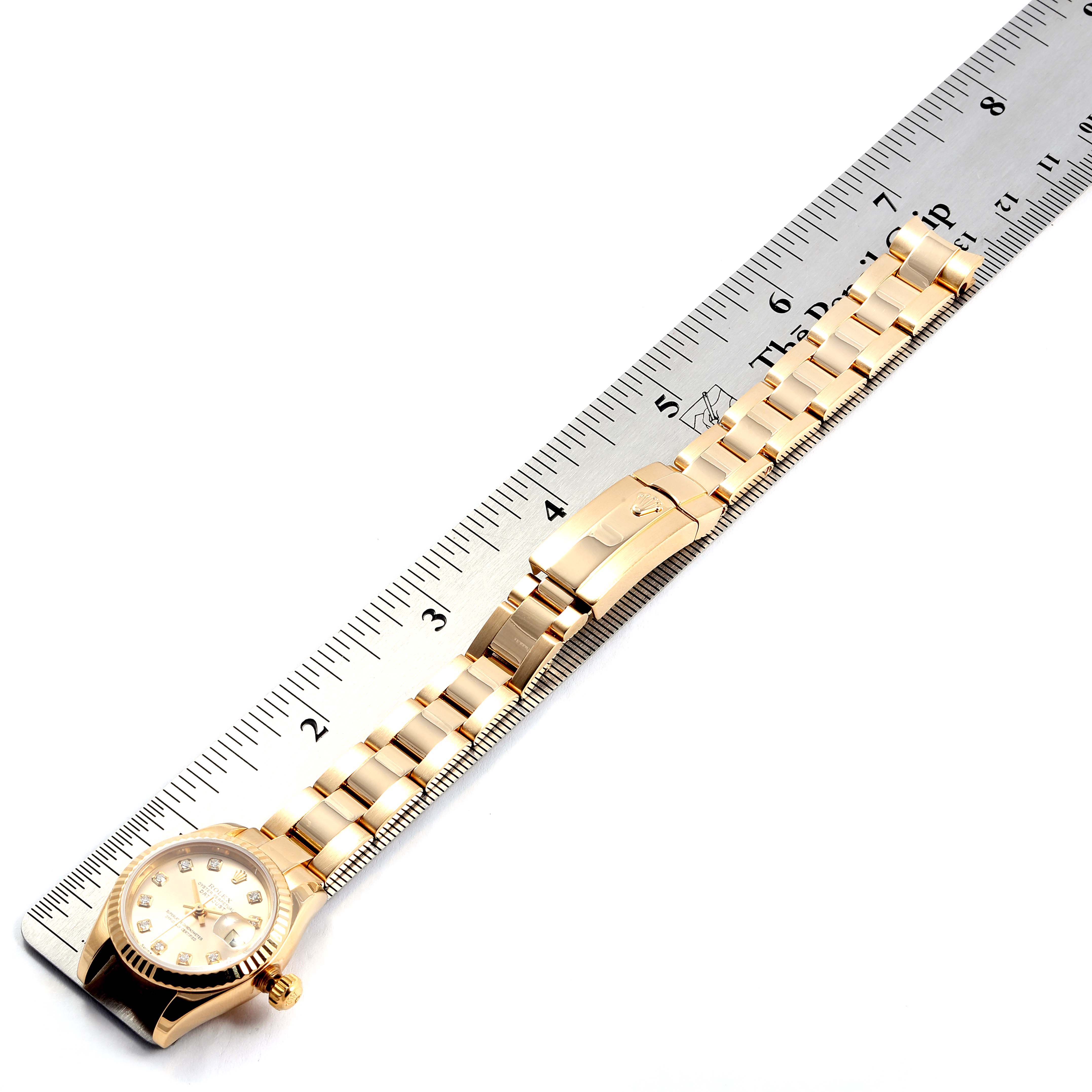 The image shows a Rolex President 179178 Women
s Yellow Gold Champagne Dial 179178 Women
s Yellow Gold Champagne Dial model watch laid flat beside a ruler, revealing the watch
s face, bracelet, and clasp.