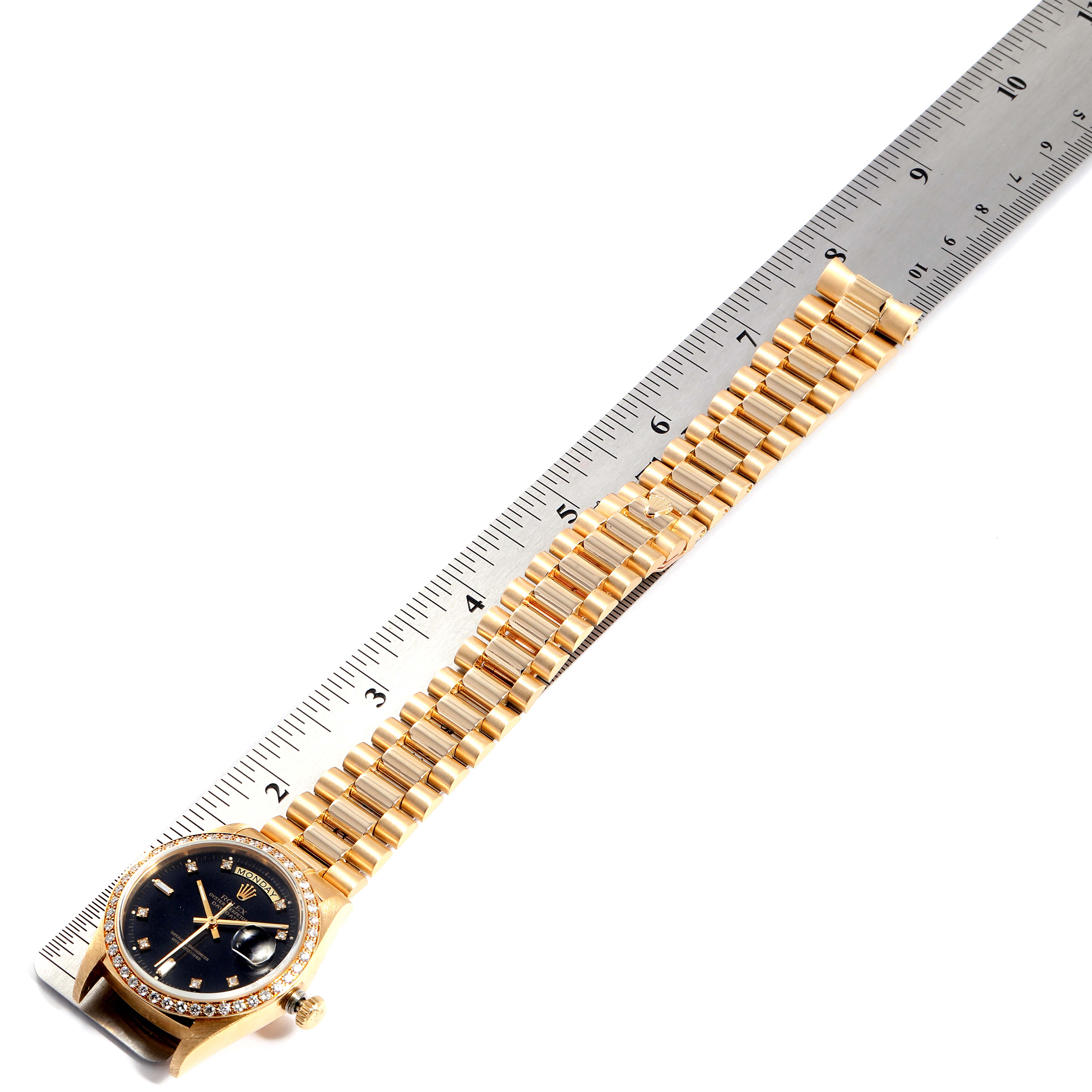 The image shows a Rolex President 18038 Men
s Yellow Gold Black Dial 18038 Men
s Yellow Gold Black Dial model watch laid flat alongside a ruler, highlighting its gold bracelet and black watch face.