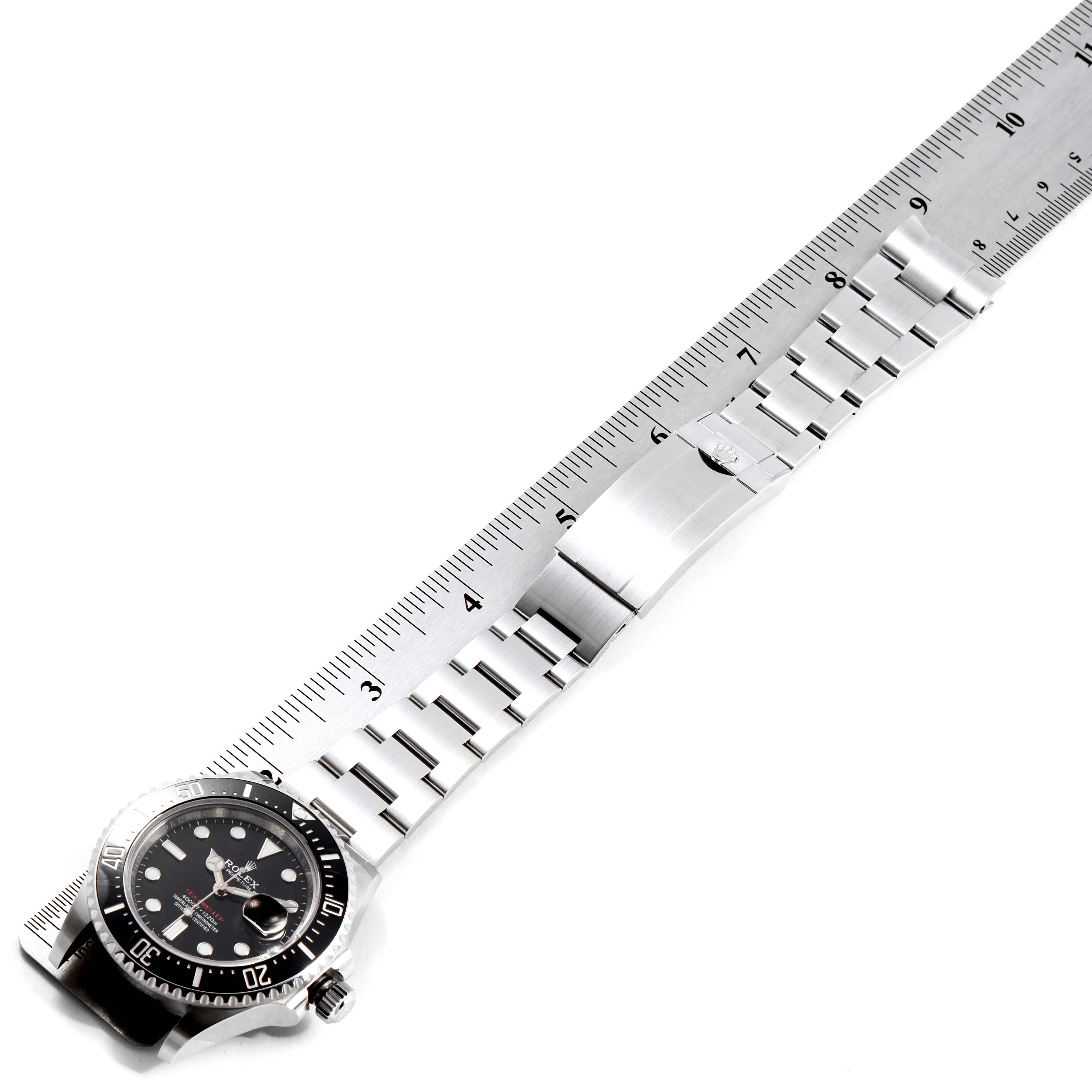 The image shows the side angle of a Rolex Sea-Dweller 126600 Men
s Stainless Steel Black Dial 126600 Men
s Stainless Steel Black Dial watch, focusing on the dial, bezel, and metal bracelet positioned next to a ruler.