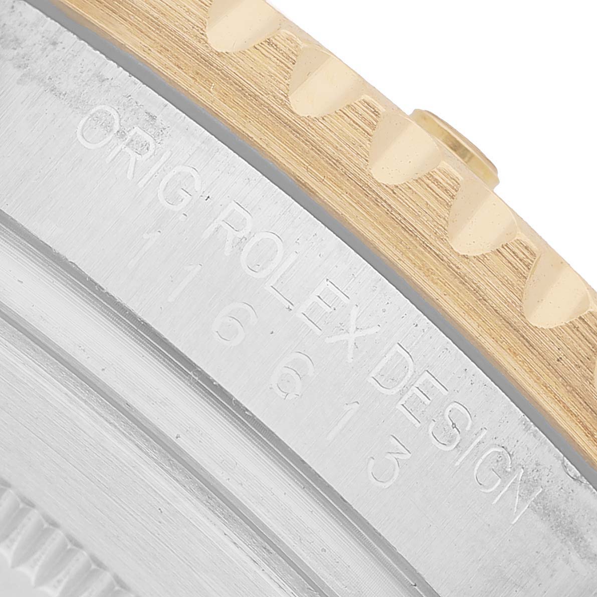 The image shows the edge of a Rolex Submariner 116613 Men's Steel and Gold (two tone) Black Dial's casing with part of the bezel and engraved text.