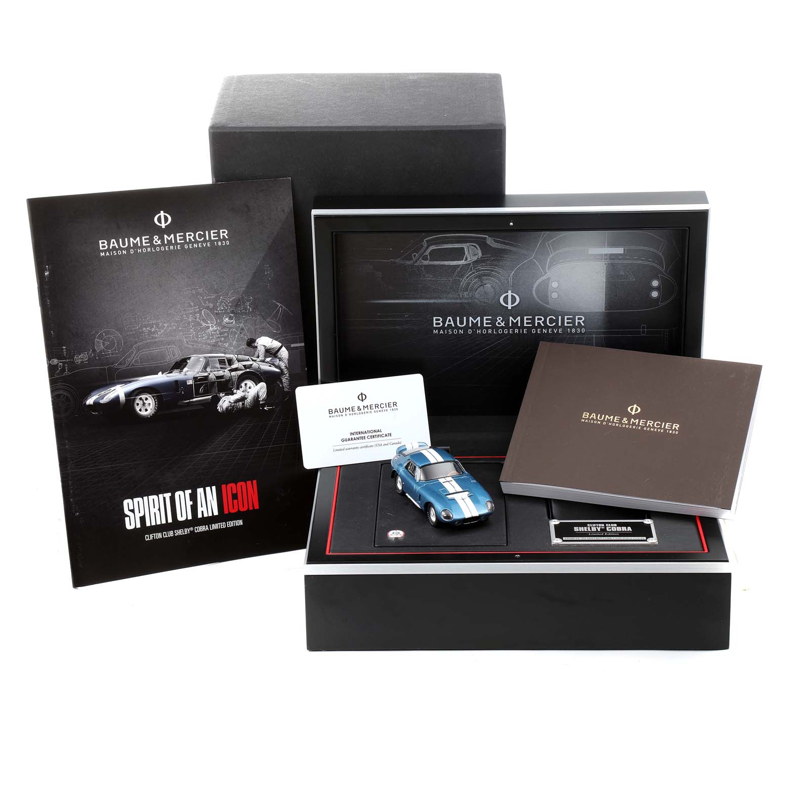 The image shows the packaging and accessories of a Baume & Mercier Clifton M0A10342 Men's Stainless Steel Silver Dial M0A10342 Men's Stainless Steel Silver Dial watch, including a model car, certificate, and booklet.