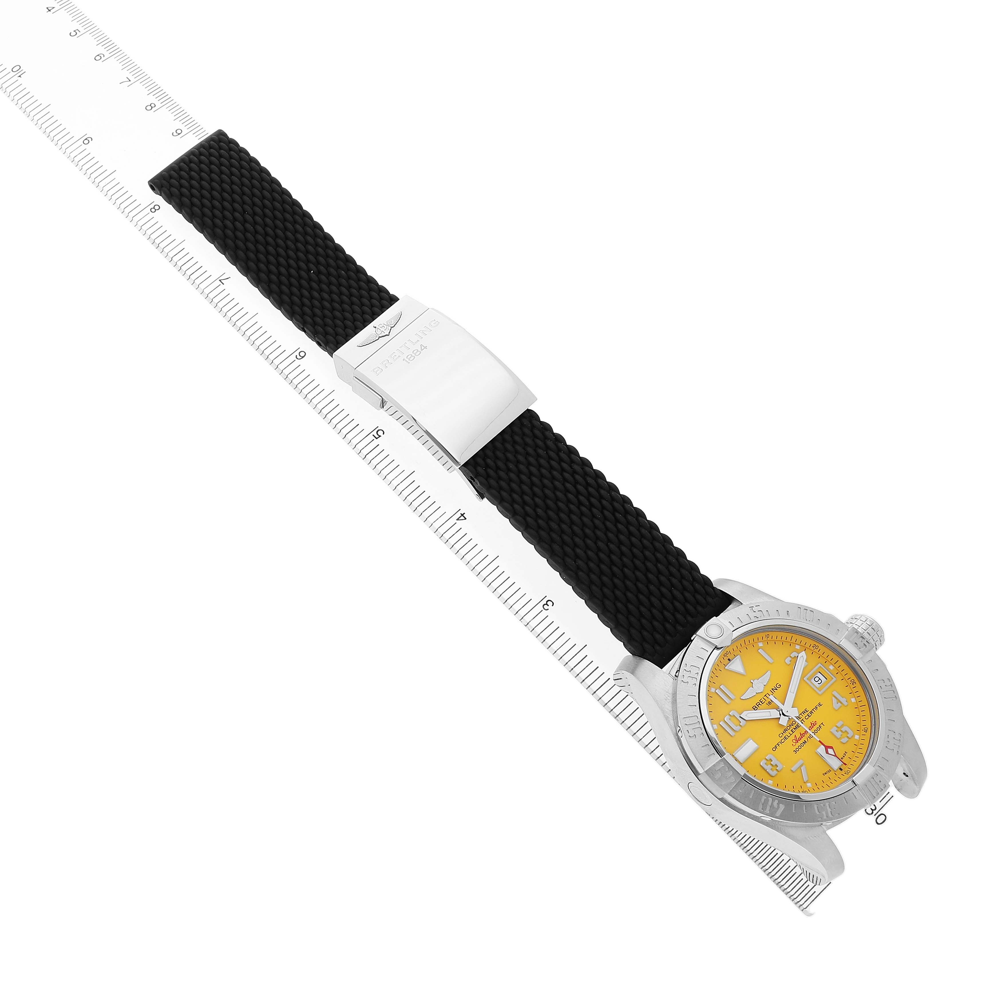 The Breitling Avenger A17331 Men's Stainless Steel Yellow Dial watch is displayed at an oblique angle, showing its face, bezel, crown, and a black strap beside a ruler.
