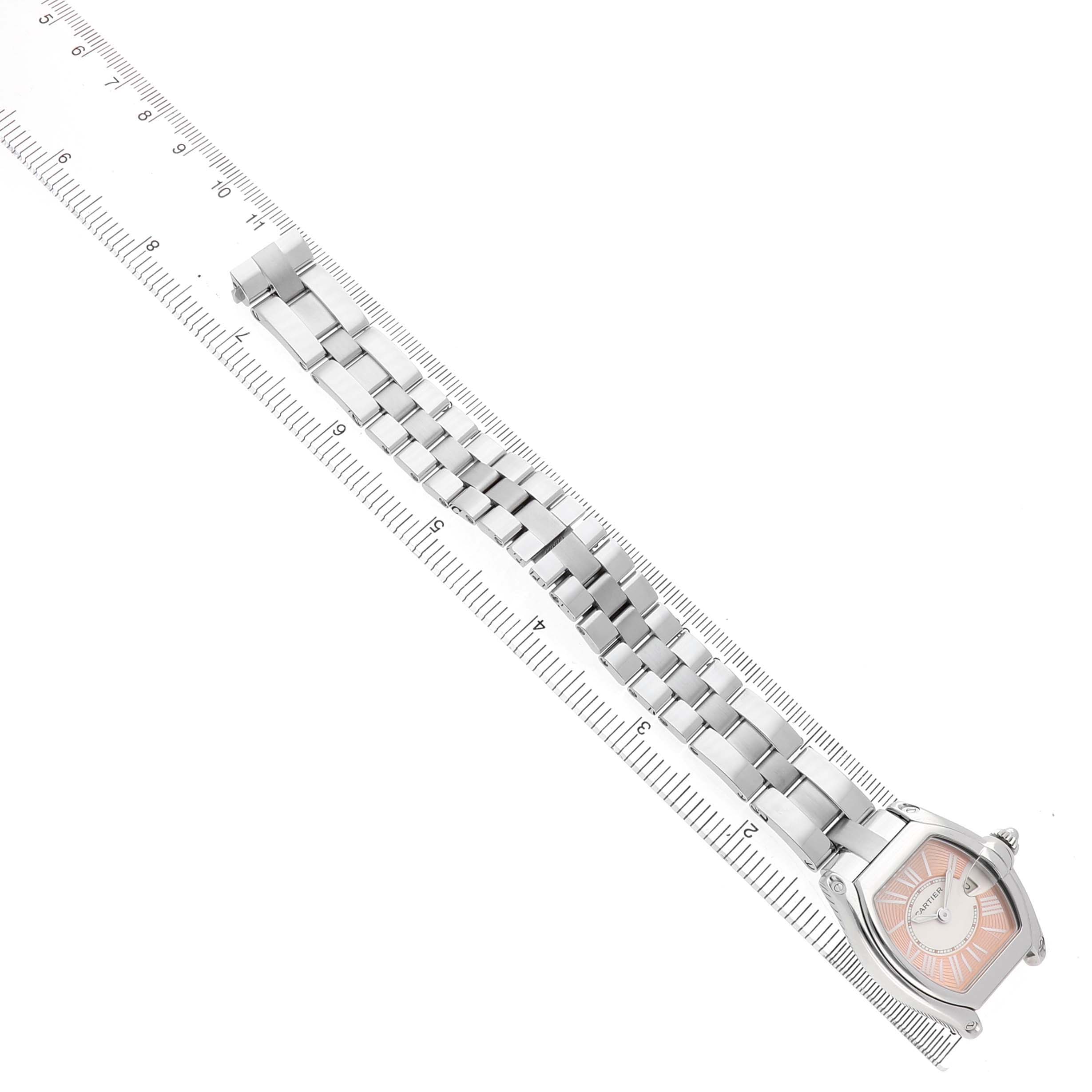 The Cartier Roadster W62017V3 Women's Stainless Steel Pink Dial watch is shown at an angle, highlighting its face, bezel, and metal bracelet next to a ruler.