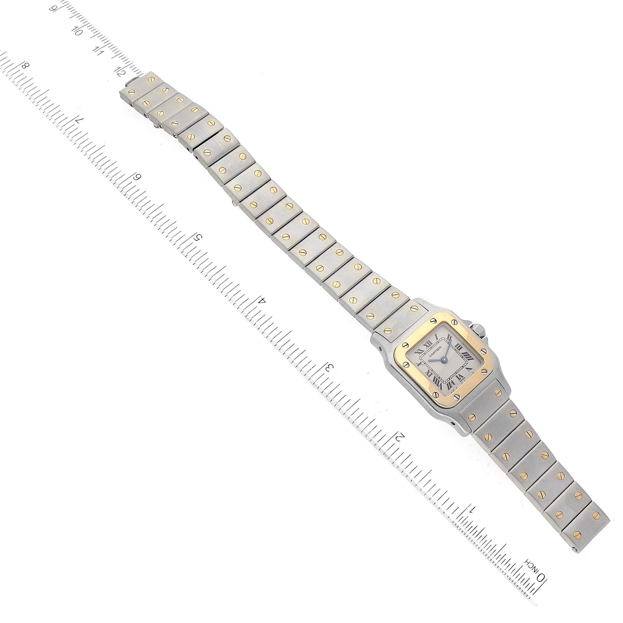 The image shows an overhead view of a Cartier Santos W20012C4 Women's Steel and Gold (two tone) Silver Dial W20012C4 Women's Steel and Gold (two tone) Silver Dial model watch, highlighting its face, bezel, and full bracelet next to a ruler.