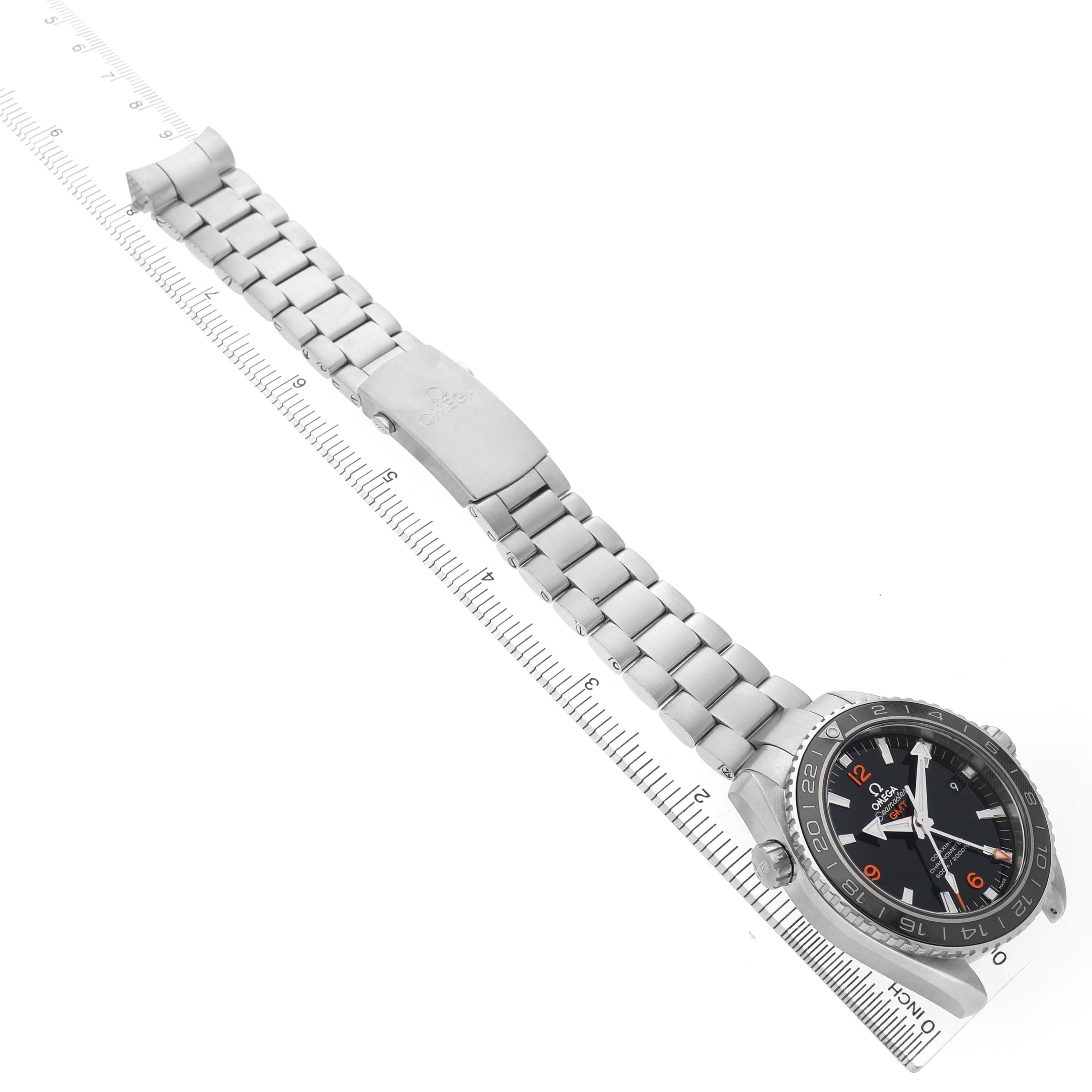 The Omega Planet Ocean 232.30.44.22.01.002 Men's Stainless Steel Black Dial watch is shown at an angle displaying the face, bezel, bracelet, and clasp positioned along a ruler for scale.