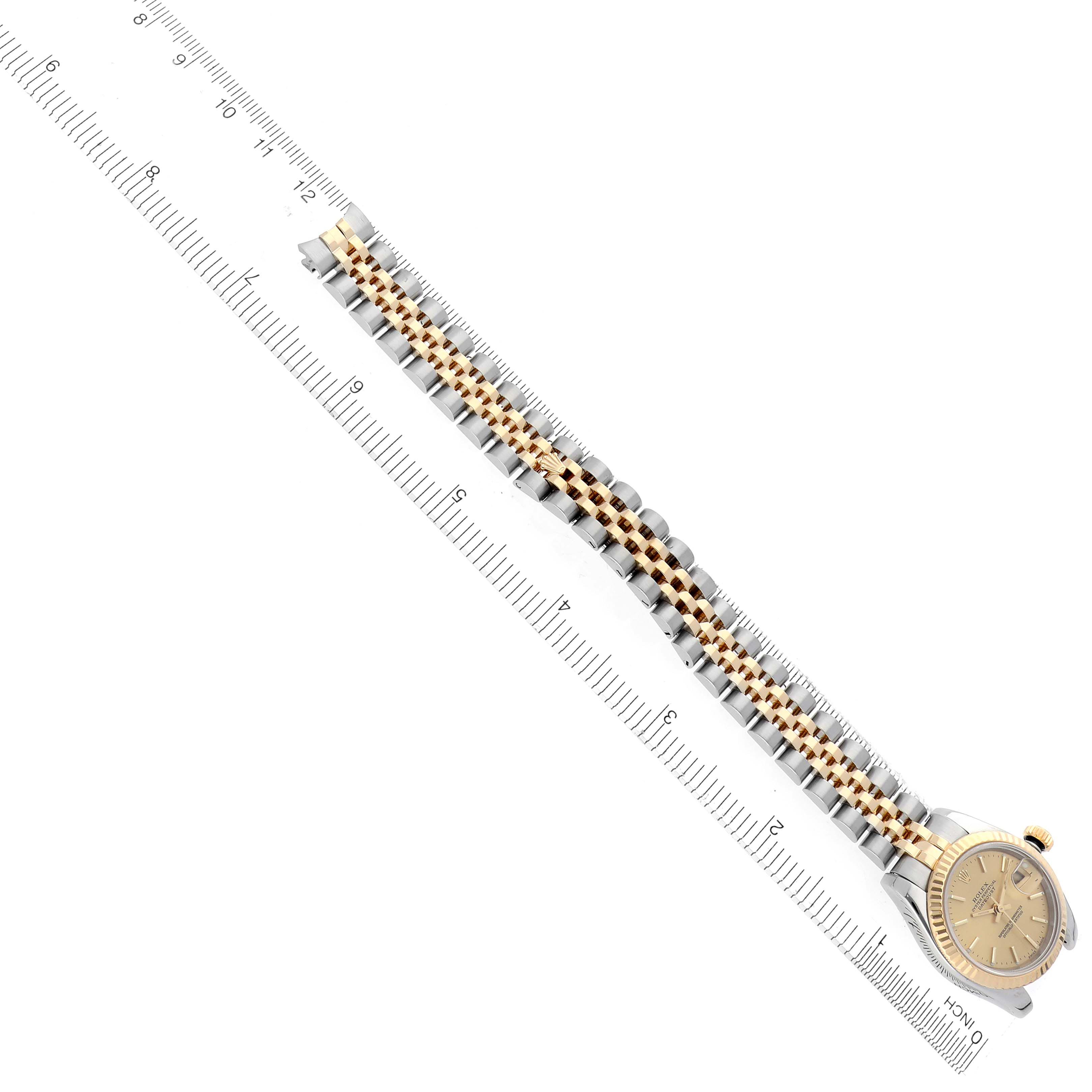 The Rolex Datejust 179173 Women's Steel and Gold (two tone) Champagne Dial 179173 Women's Steel and Gold (two tone) Champagne Dial watch is shown at a diagonal angle, featuring the bracelet and a partial view of the dial beside a ruler.