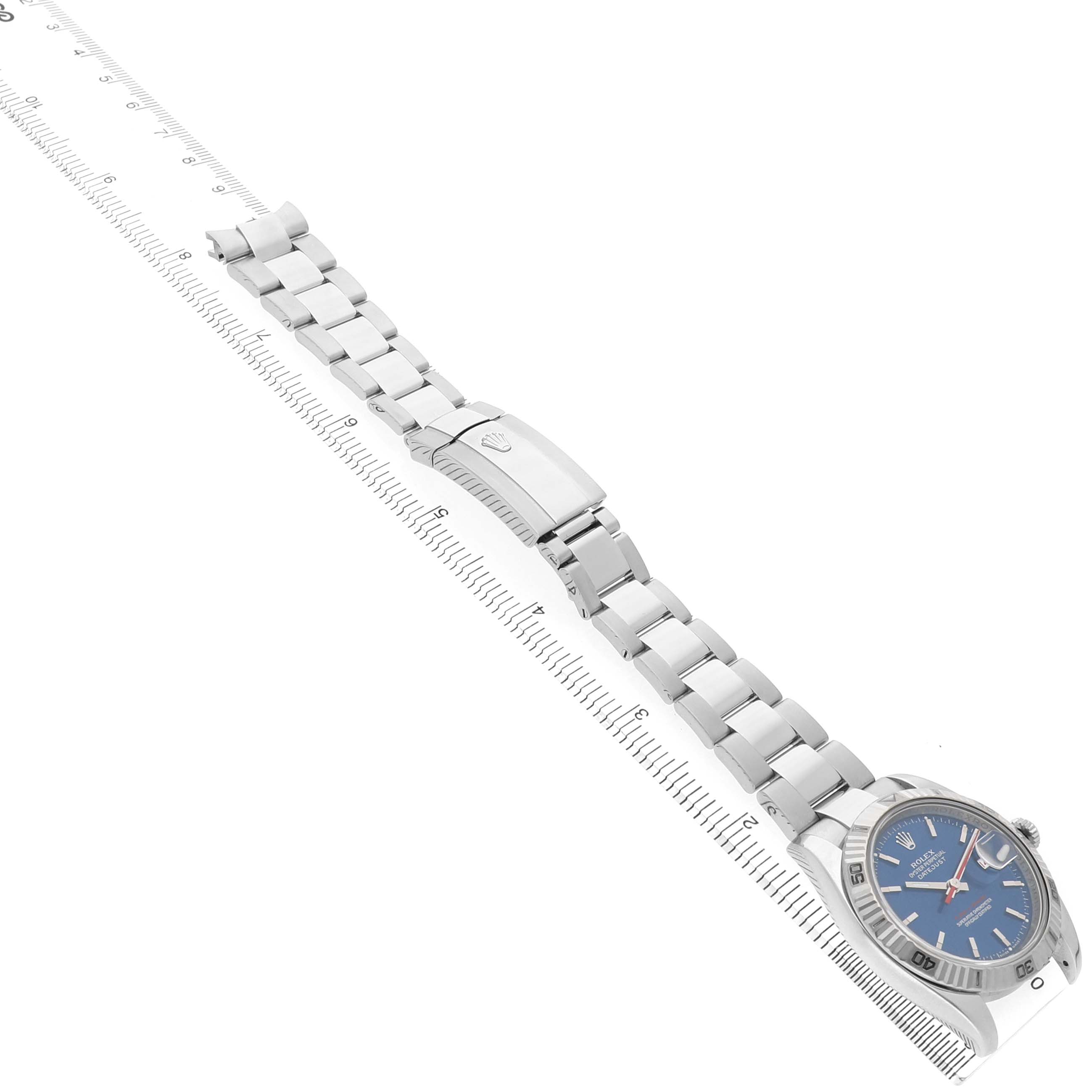 The Rolex Turn-o-Graph 116264 Men's Stainless Steel Blue Dial watch is displayed from an overhead angle, showing its face, bezel, and metal bracelet lying flat next to a ruler.