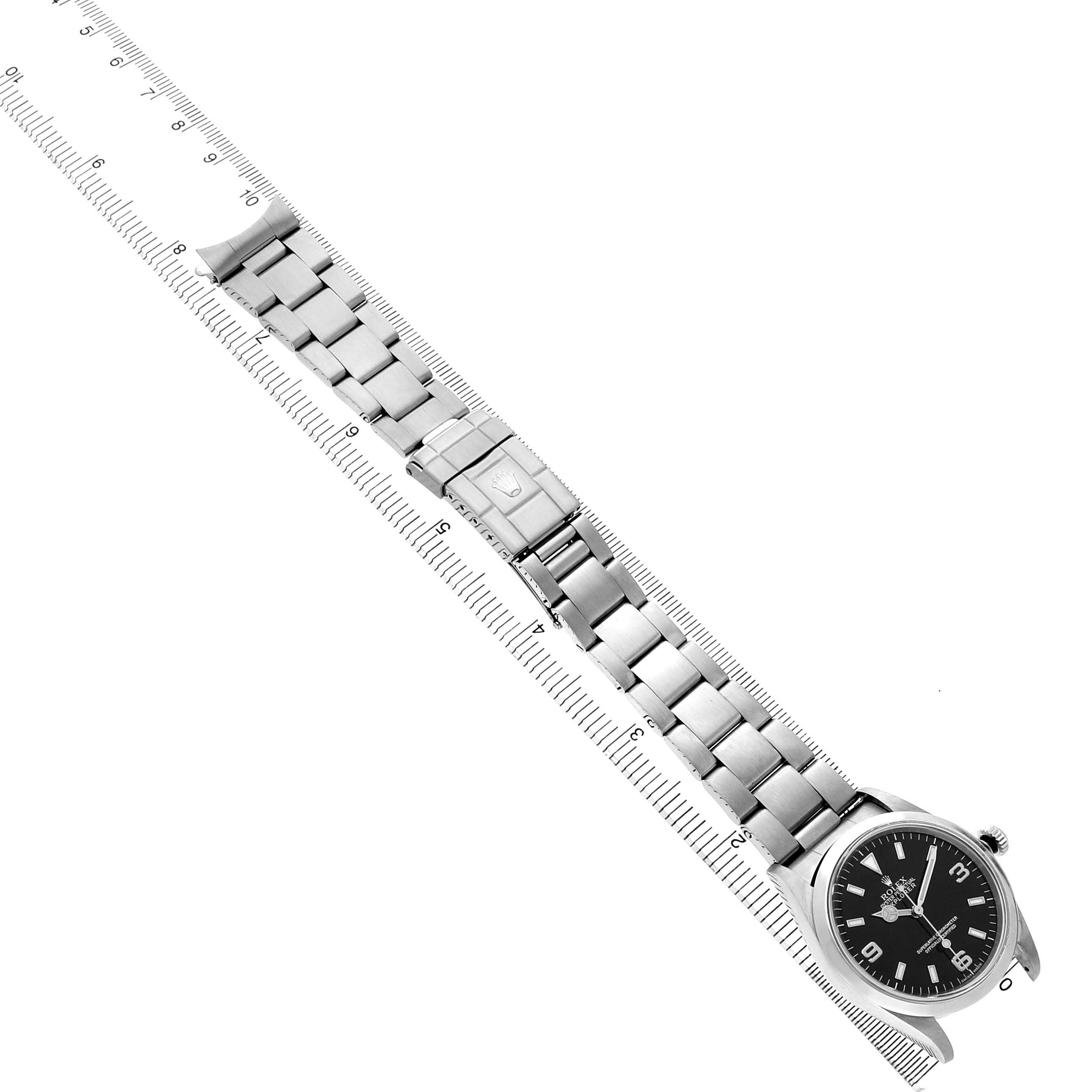 The Rolex Explorer 14270 Men's Stainless Steel Black Dial watch is shown from a top-down angle, displaying its face, bracelet, and clasp alongside a ruler for scale.