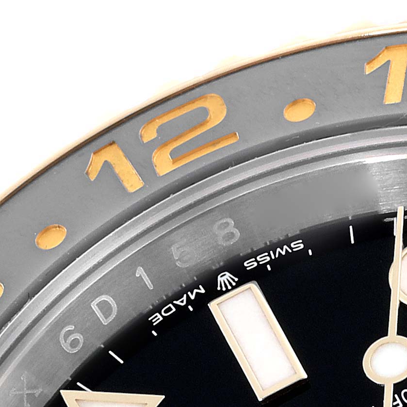 This close-up image of the Rolex GMT-Master 126713GRNR Men's Steel and Gold (two tone) Black Dial 126713GRNR Men's Steel and Gold (two tone) Black Dial shows the bezel and a portion of the dial, including the "12" marking and part of the "SWISS MADE" text.