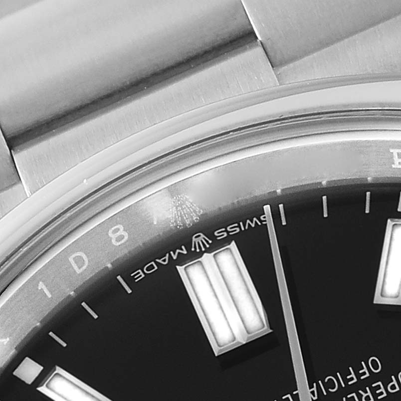 This close-up image of the Rolex Oyster Perpetual 126000 Men
s Stainless Steel Black Dial 126000 Men
s Stainless Steel Black Dial watch shows part of the dial, bracelet, and bezel.