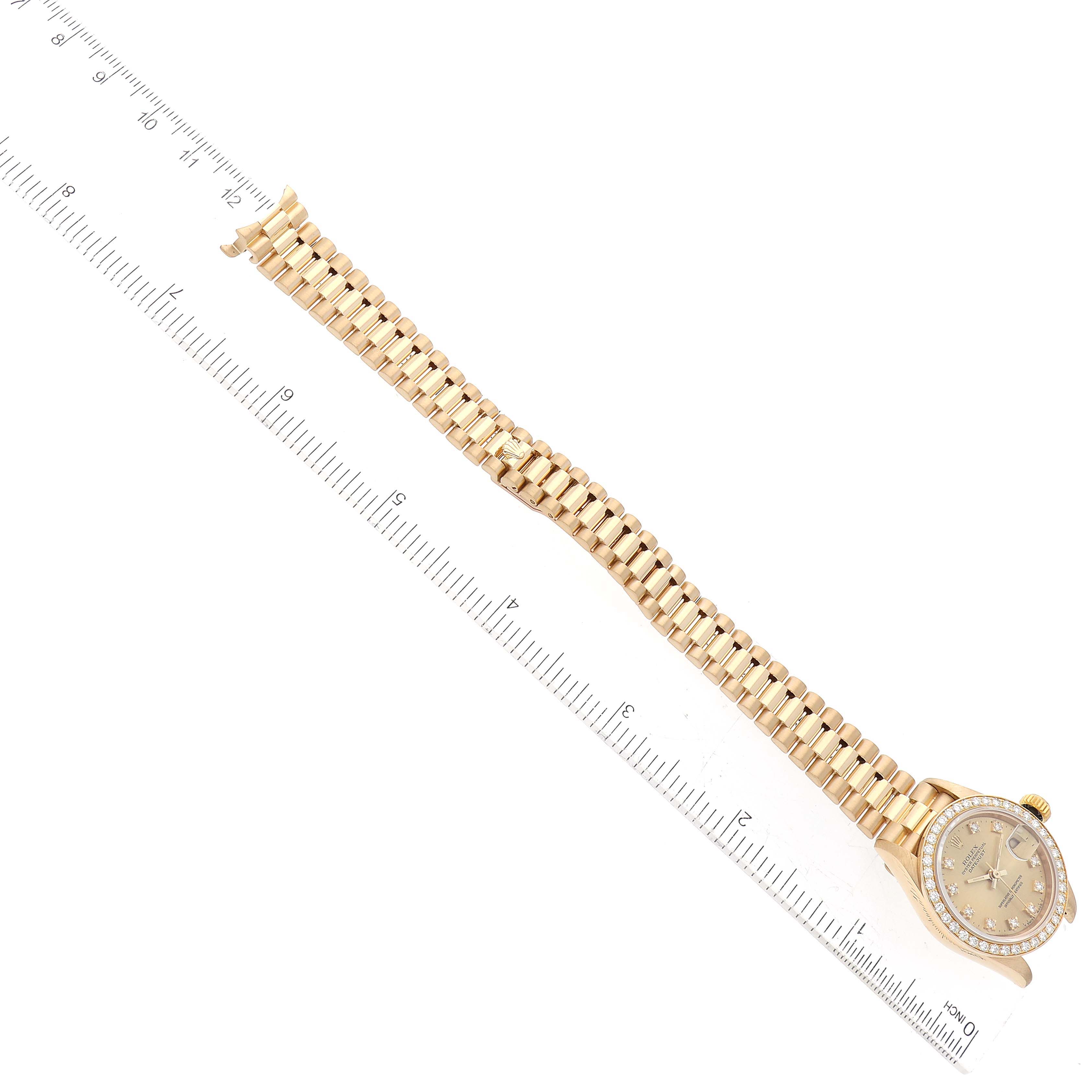 The image shows a Rolex President 69138G Women
s Yellow Gold Champagne Dial 69138G Women
s Yellow Gold Champagne Dial model watch laid flat with its bracelet, next to a ruler for measuring length.