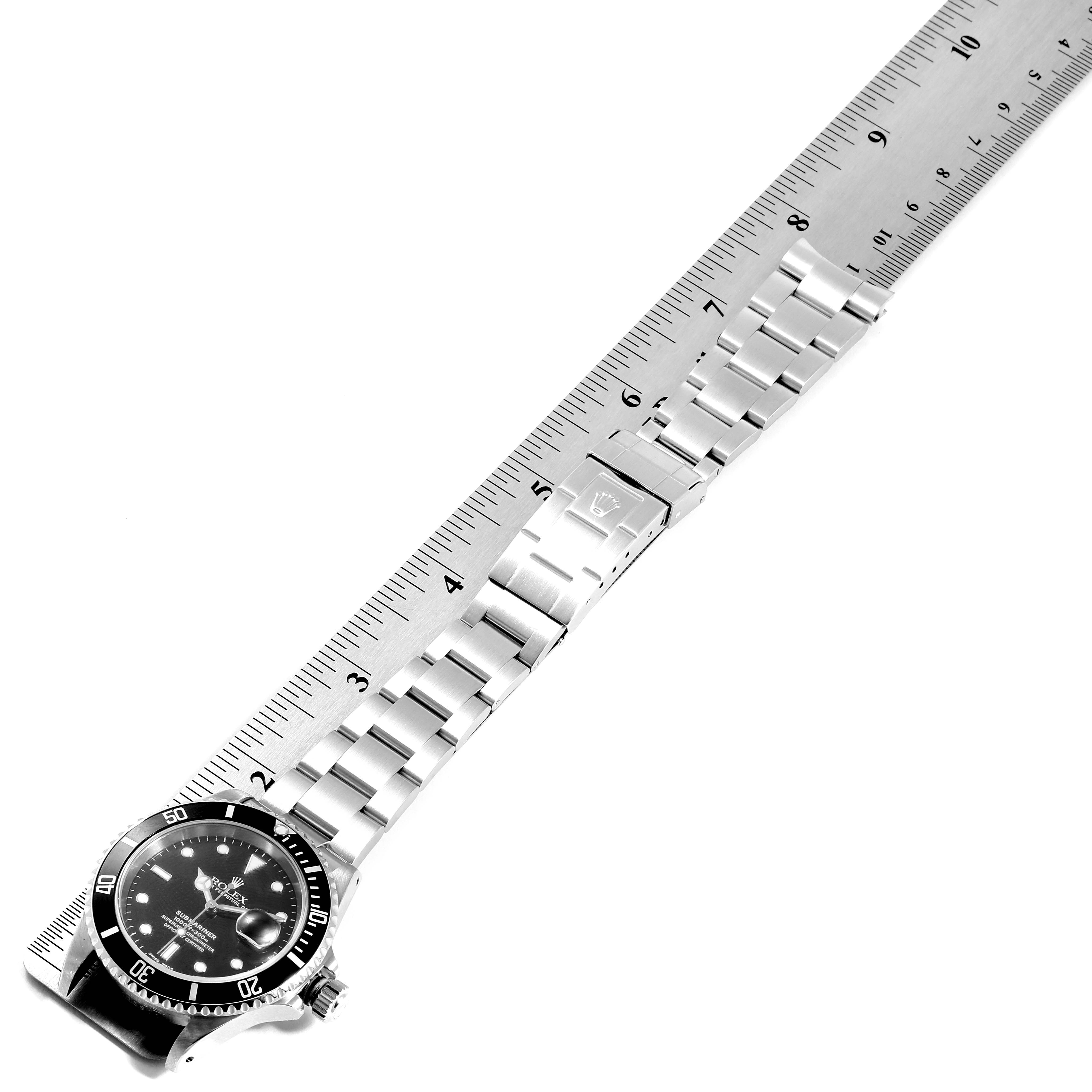 The image shows a Rolex Submariner 16610 Men
s Stainless Steel Black Dial 16610 Men
s Stainless Steel Black Dial watch positioned alongside a ruler, highlighting its stainless steel bracelet and clasp.
