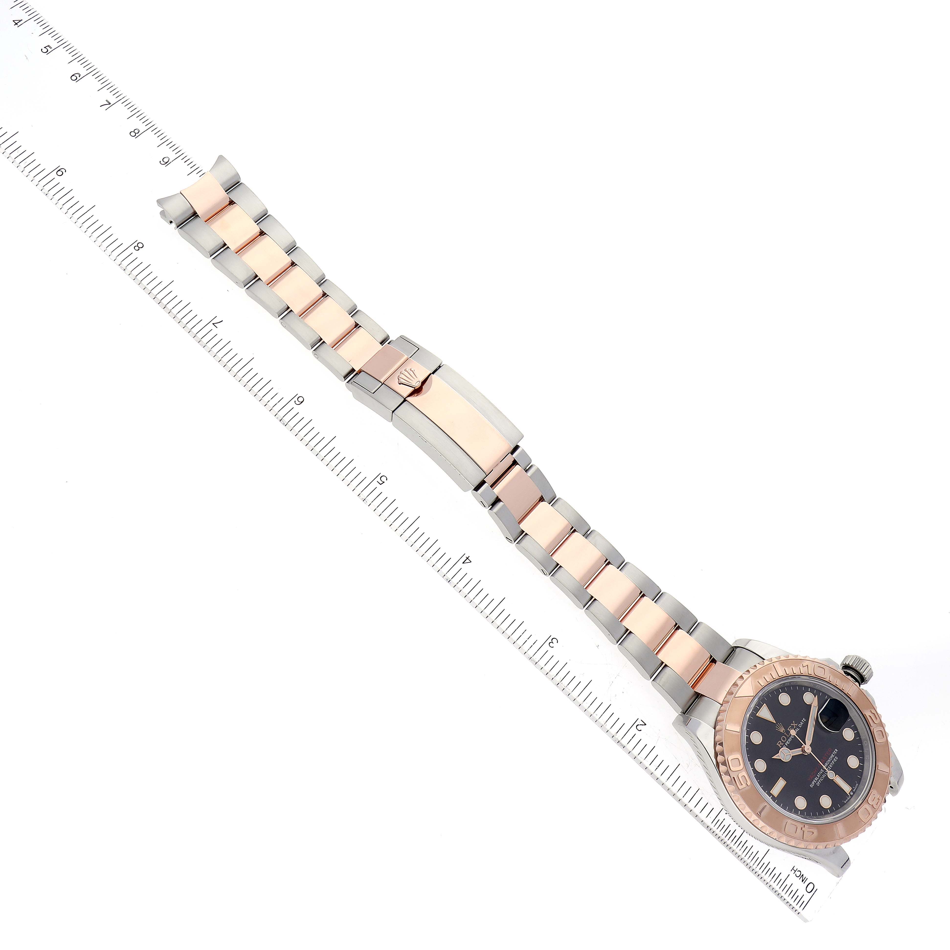 The Rolex Yacht-Master 126621 Men's Steel and Gold (two tone) Black Dial 126621 Men's Steel and Gold (two tone) Black Dial watch is displayed at an overhead angle, showing the full bracelet, clasp, and face with measuring rulers beside it.