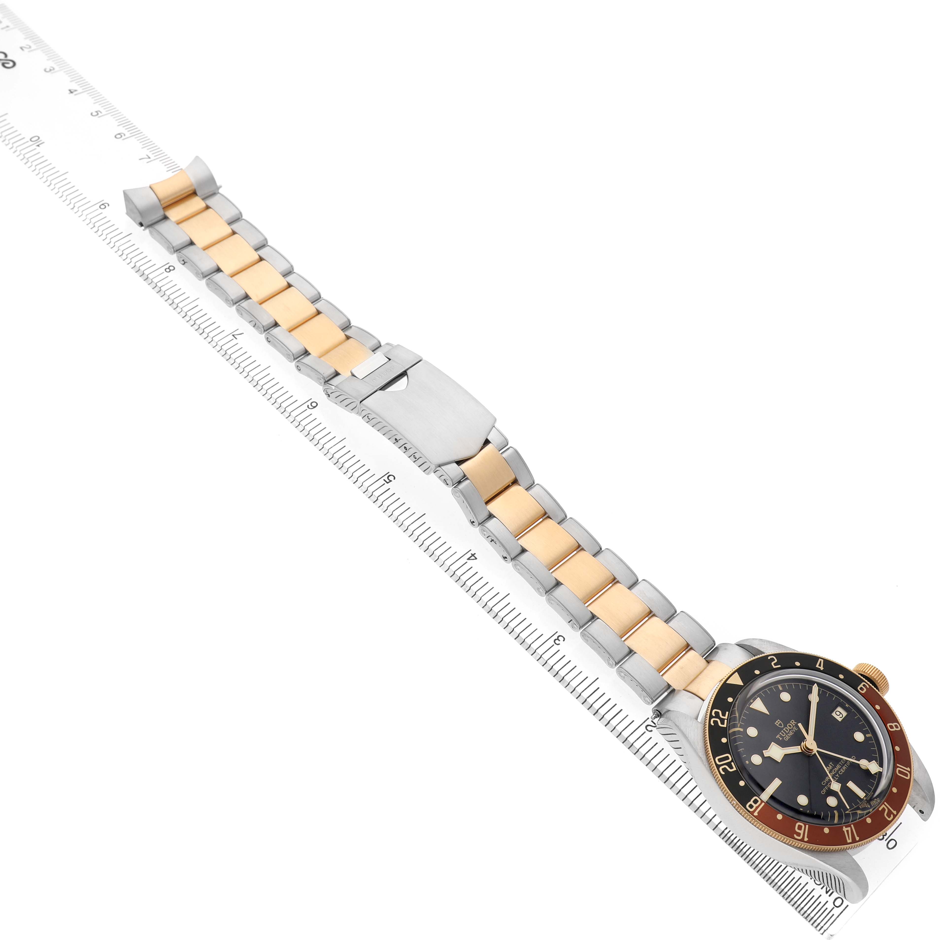 The Tudor Heritage Black Bay 79833MN Men's Steel and Gold (two tone) Black Dial watch is shown at an angle, displaying its face, two-tone bracelet, and clasp on a ruler for scale.