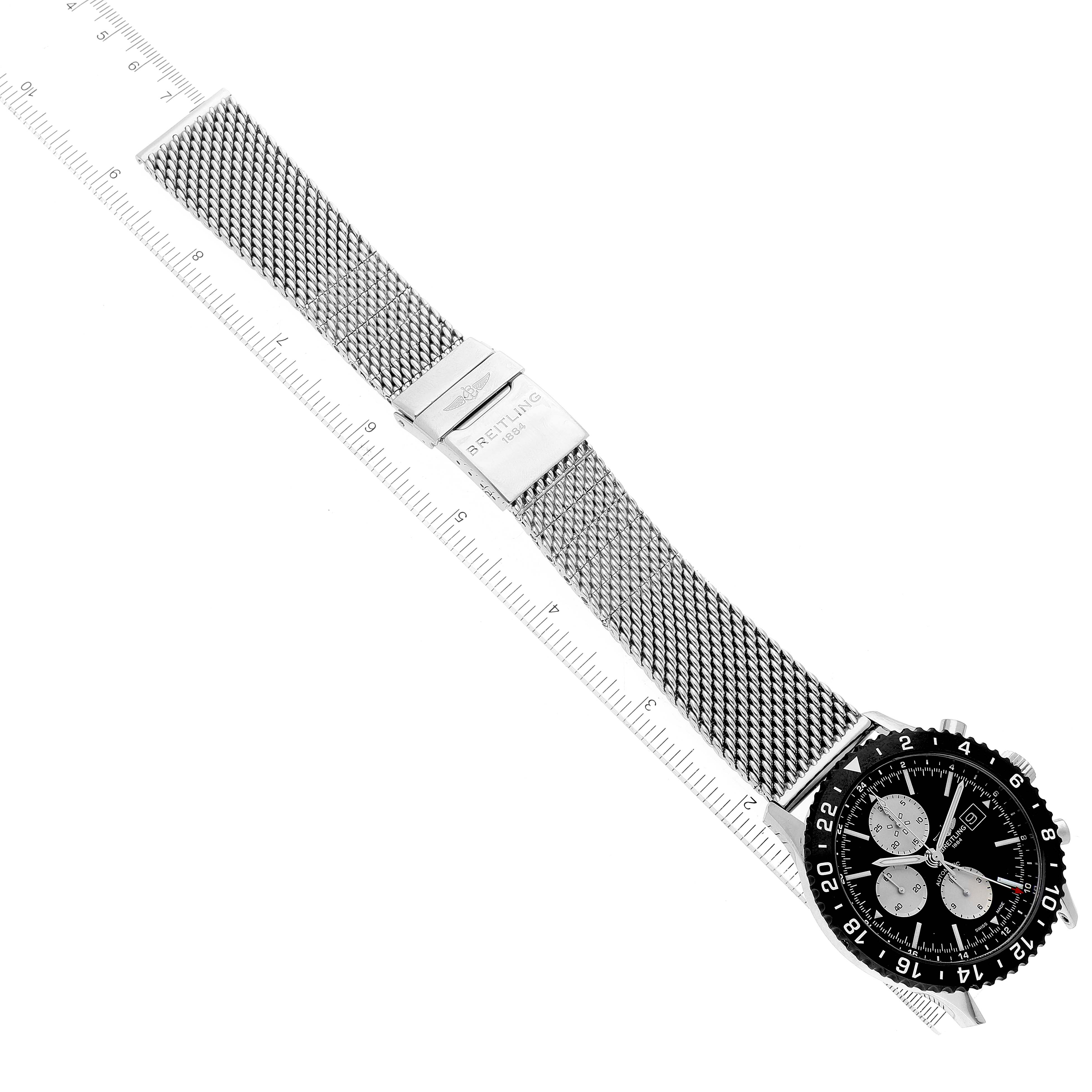 The image shows a full view of the Breitling Chronoliner Y2431012/BE10 Men's Stainless Steel Black Dial Y2431012/BE10 Men's Stainless Steel Black Dial watch lying flat with its mesh strap extended alongside a ruler.