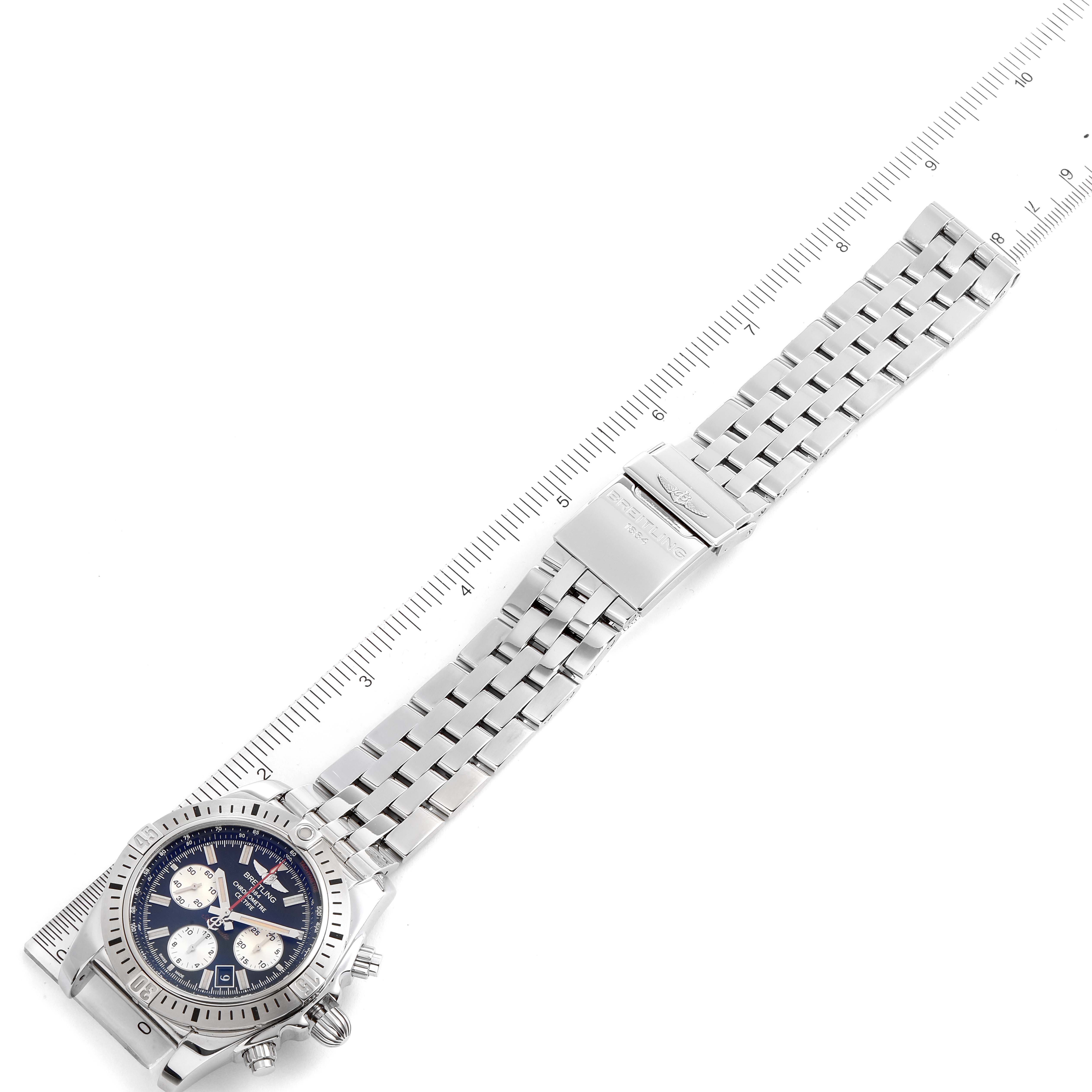 The image shows a top view of a Breitling Chronomat AB0115 Men
s Stainless Steel Black Dial AB0115 Men
s Stainless Steel Black Dial watch, displaying its face, bezel, and metal bracelet alongside a measuring ruler.