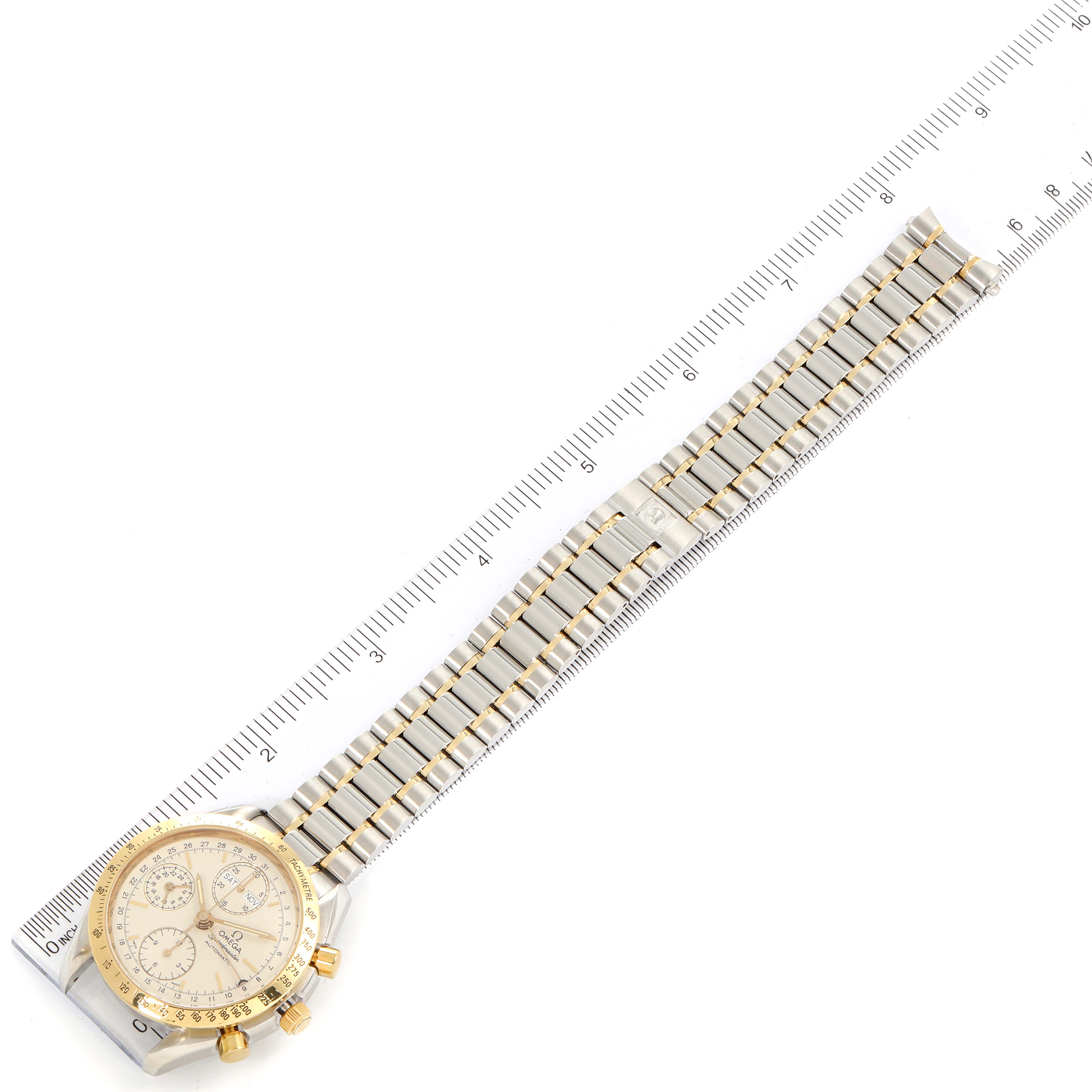 This image shows an Omega Speedmaster 3321.30.00 Men's Steel and Gold (two tone) Silver Dial 3321.30.00 Men's Steel and Gold (two tone) Silver Dial watch laid flat with its face and full bracelet visible, placed next to a ruler.