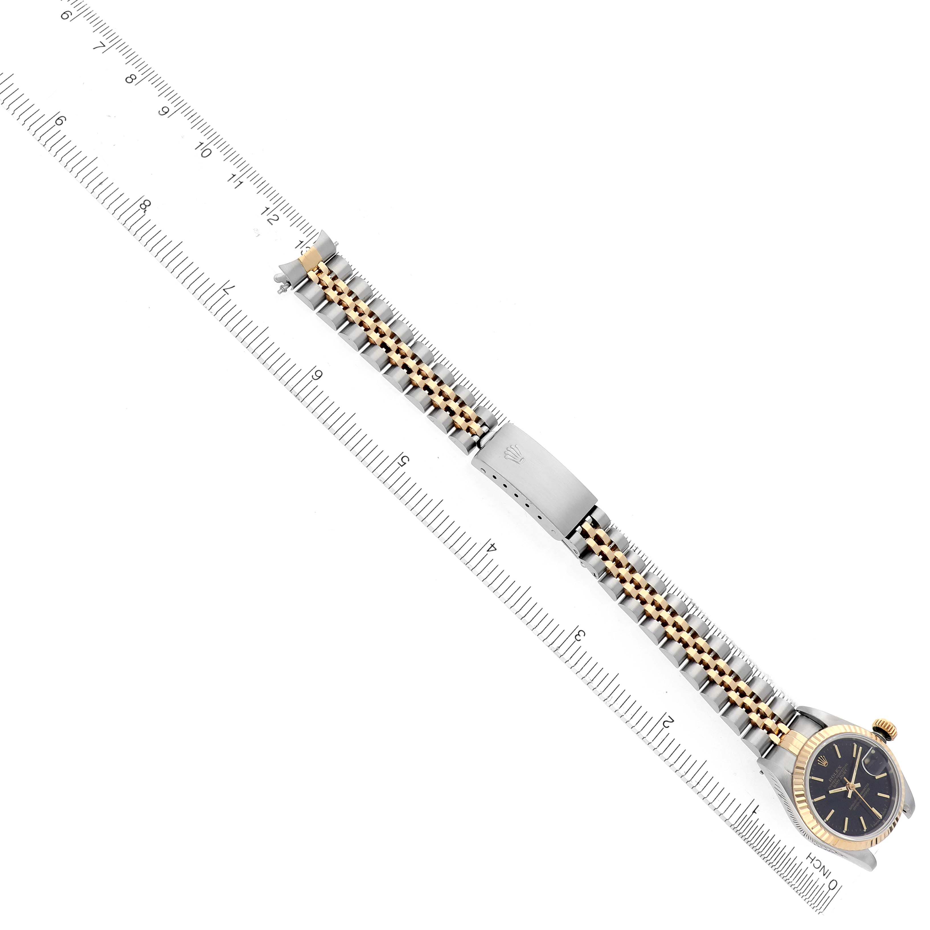 The Rolex Date 69173 Women's Steel and Gold (two tone) Black Dial 69173 Women's Steel and Gold (two tone) Black Dial watch is displayed from a side angle, showing its bracelet, clasp, bezel, and part of the dial alongside a ruler.