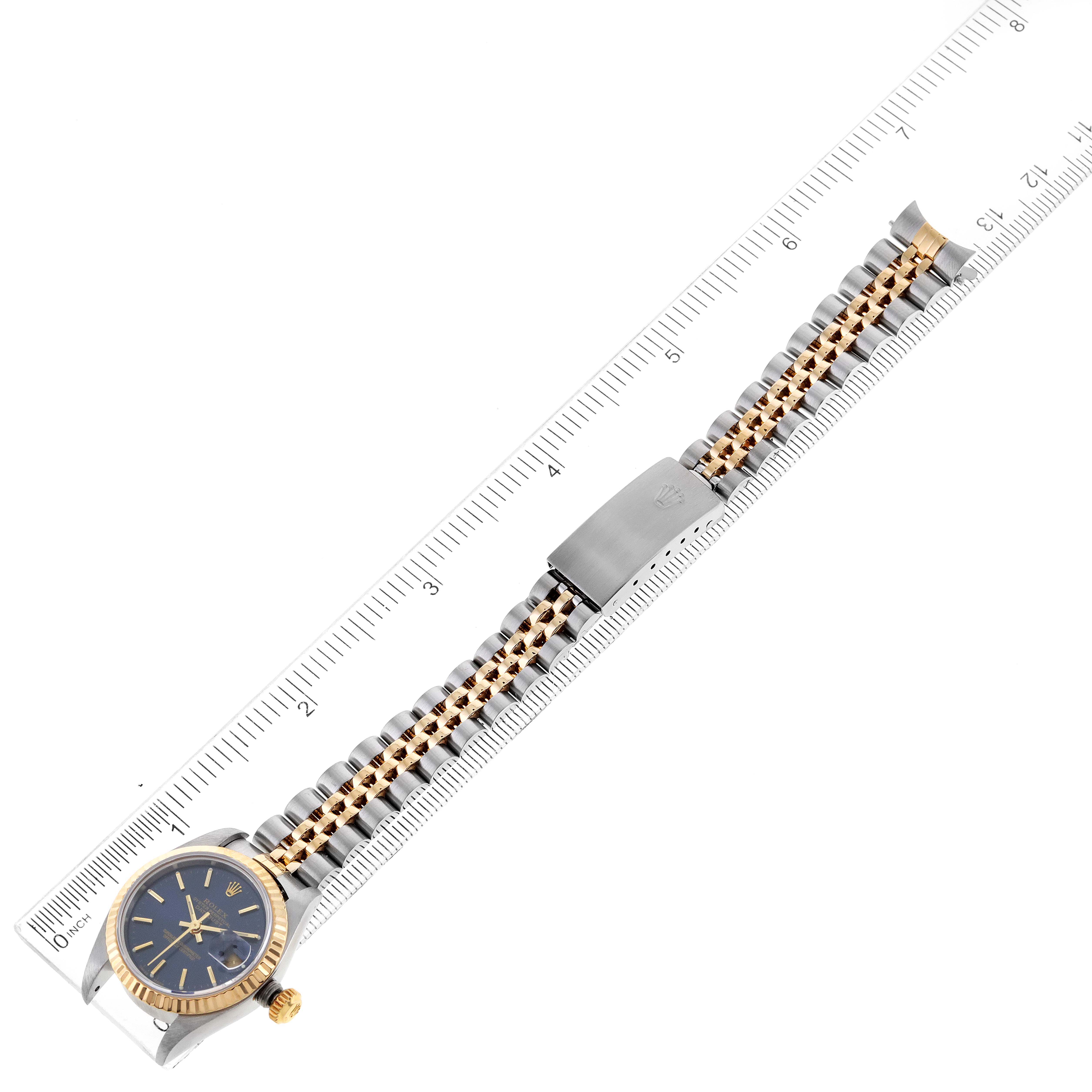 This image shows a Rolex Datejust 79173 Women's Steel and Gold (two tone) Blue Dial 79173 Women's Steel and Gold (two tone) Blue Dial watch placed alongside a ruler, highlighting its band and face at a top-down angle.