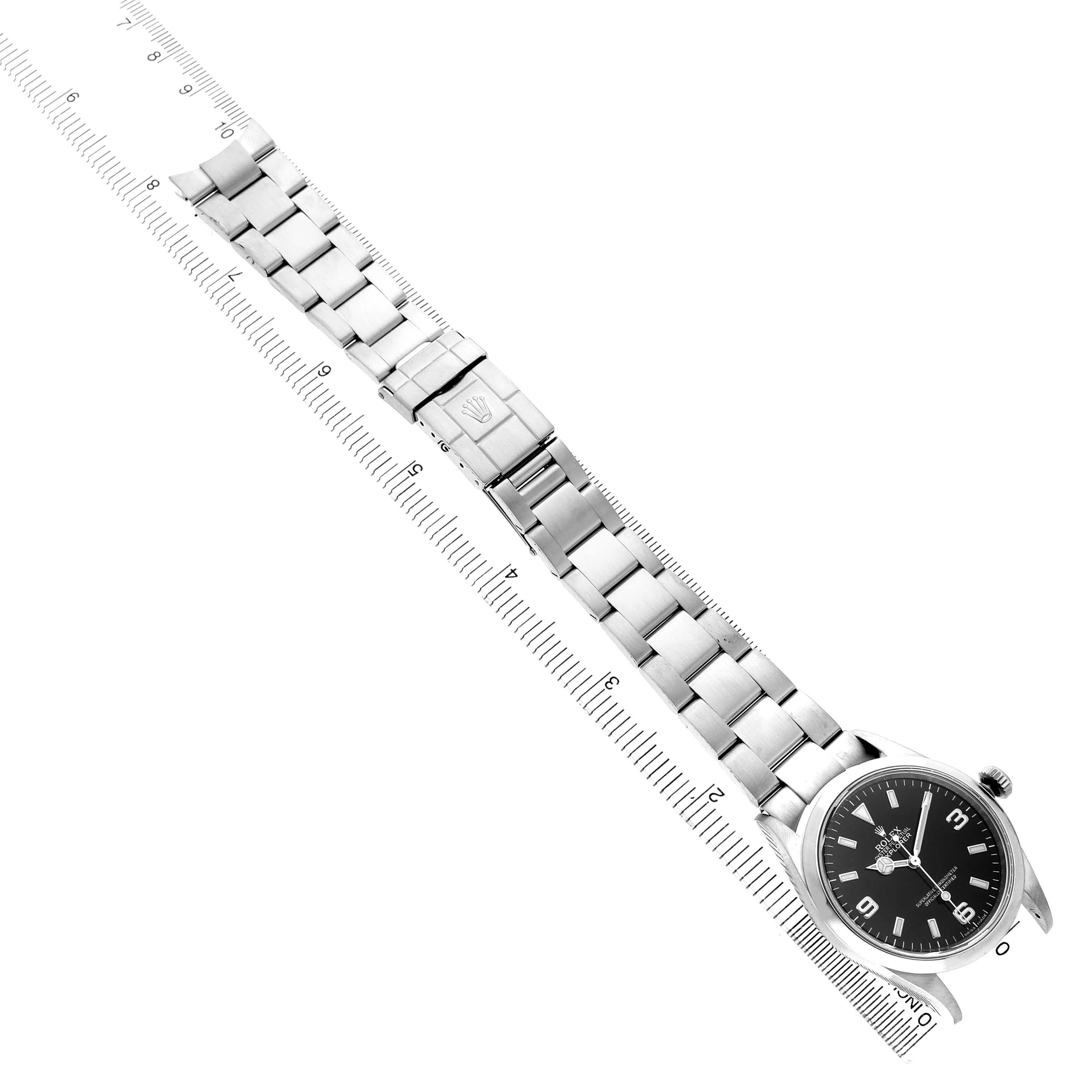 The Rolex Explorer 114270 Men's Stainless Steel Black Dial watch is displayed top-down, showing the face, bezel, bracelet, and clasp, alongside a measuring ruler.