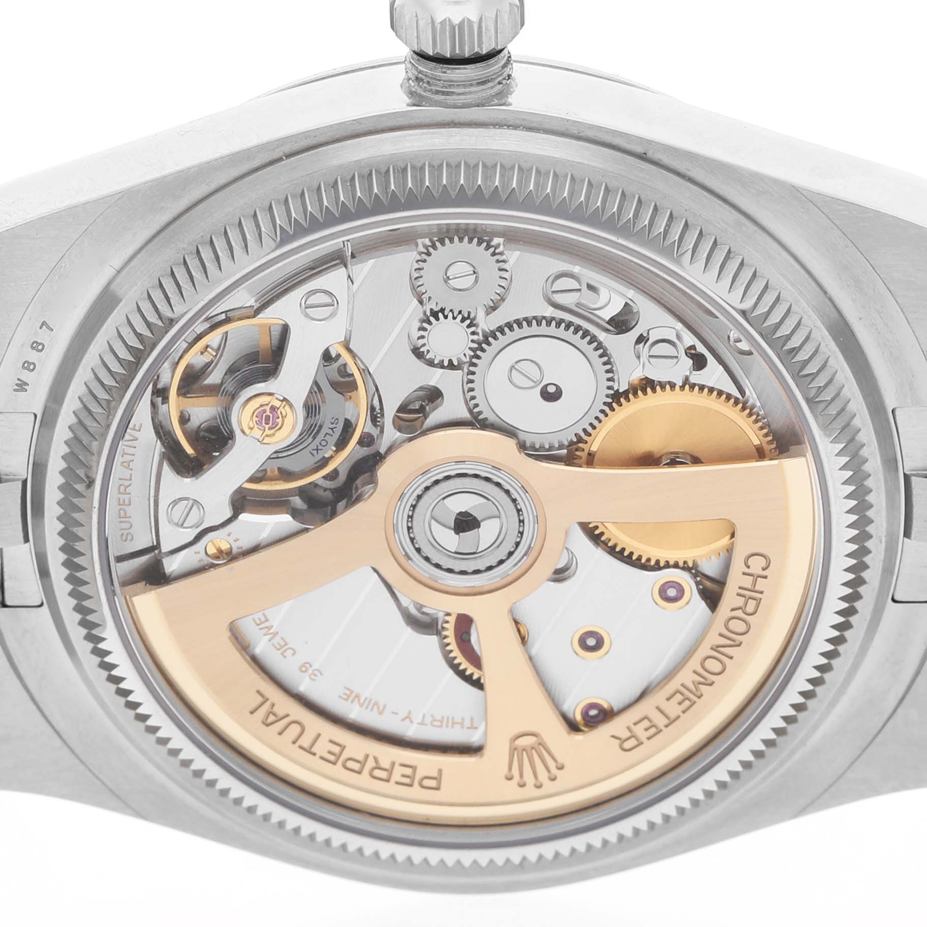 The image shows the case back of a Rolex Land‑Dweller 127234 Men's Stainless Steel White Dial, highlighting its exposed movement and intricate gears.