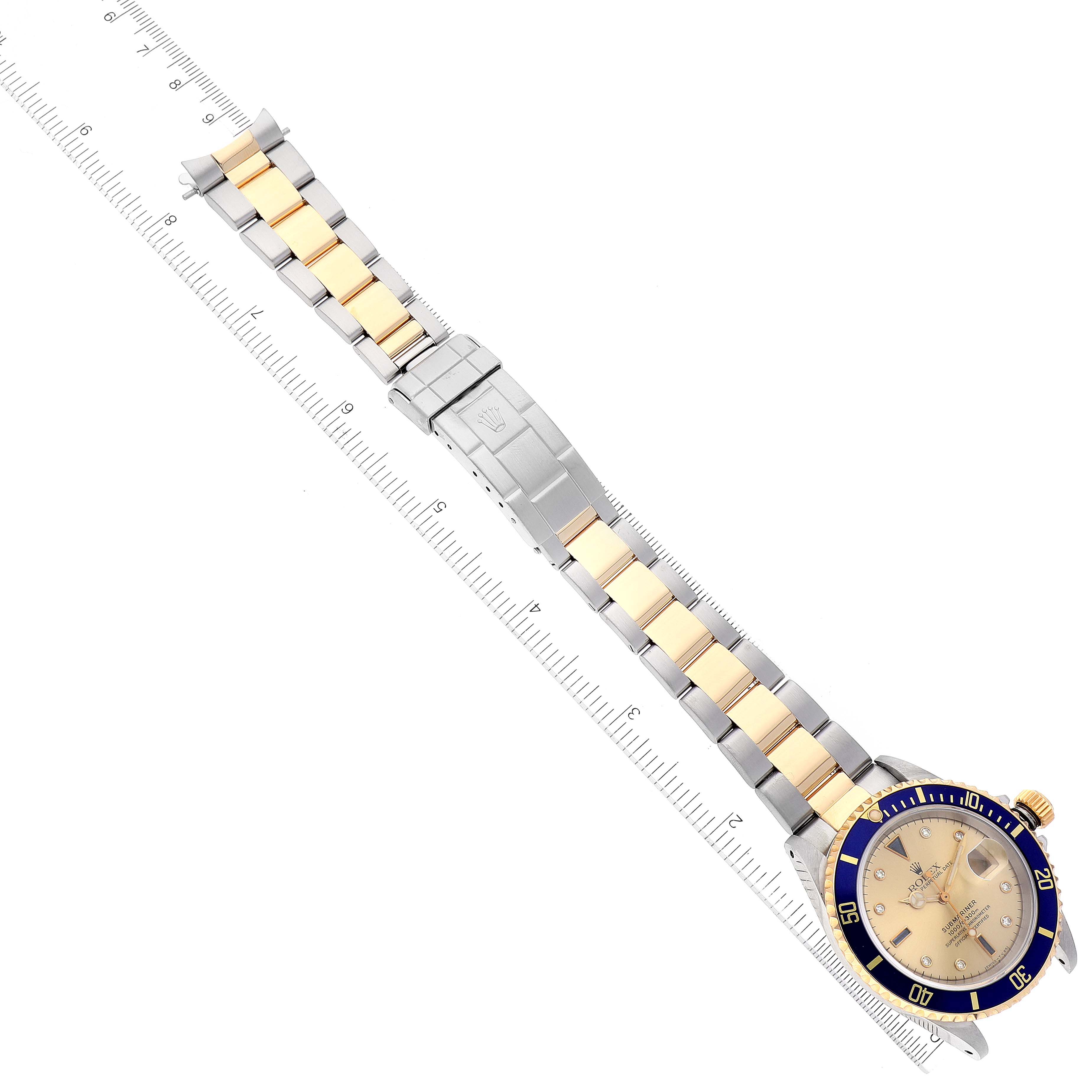 The image shows a top-down view of a Rolex Submariner 16613 Men's Steel and Gold (two tone) Champagne Dial 16613 Men's Steel and Gold (two tone) Champagne Dial watch displaying the full bracelet and face, placed alongside a measuring ruler.