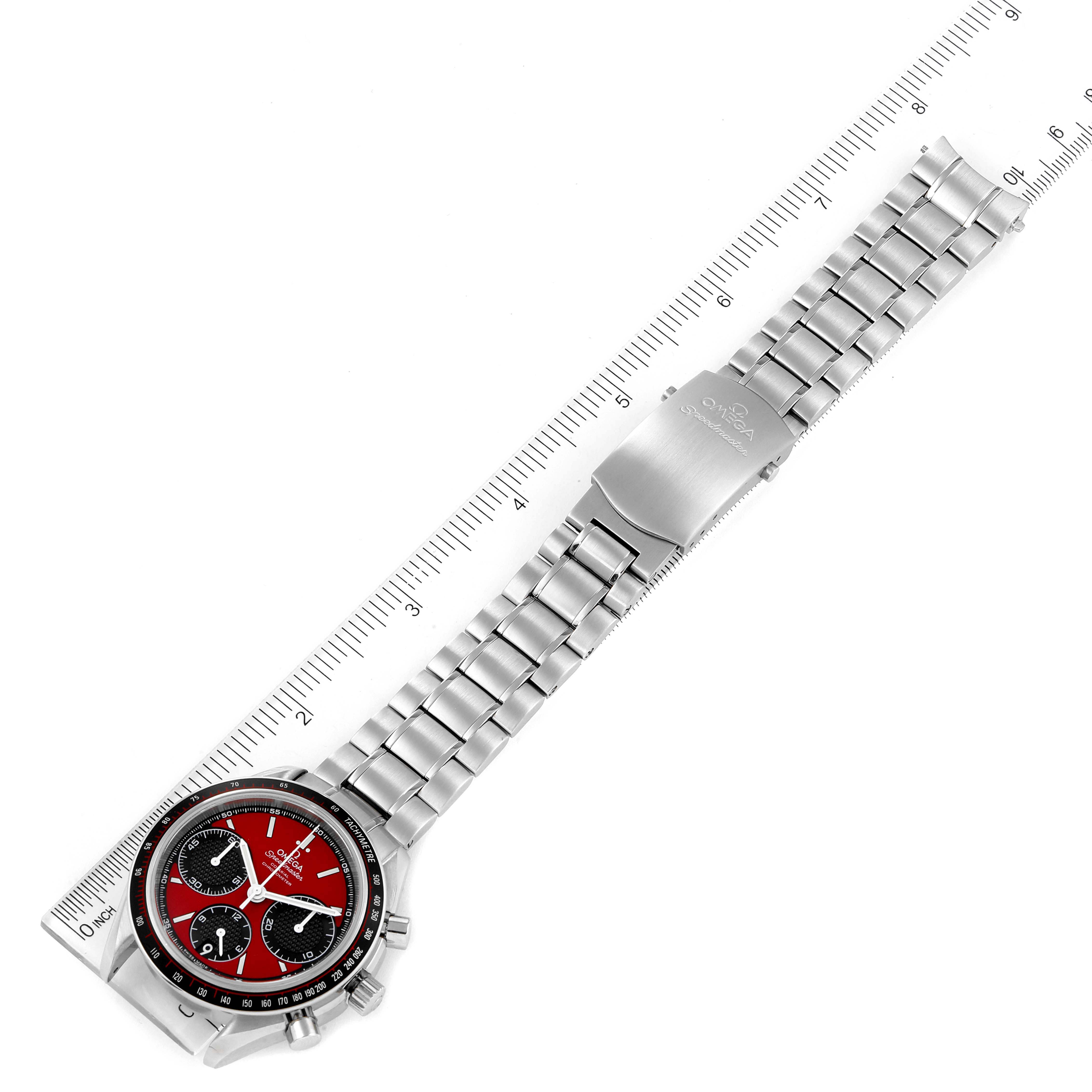 The image shows a top-down view of the Omega Speedmaster 326.30.40.50.11.001 Men's Stainless Steel Red Dial 326.30.40.50.11.001 Men's Stainless Steel Red Dial watch, highlighting its red dial, metal strap, and clasp, against a ruler.