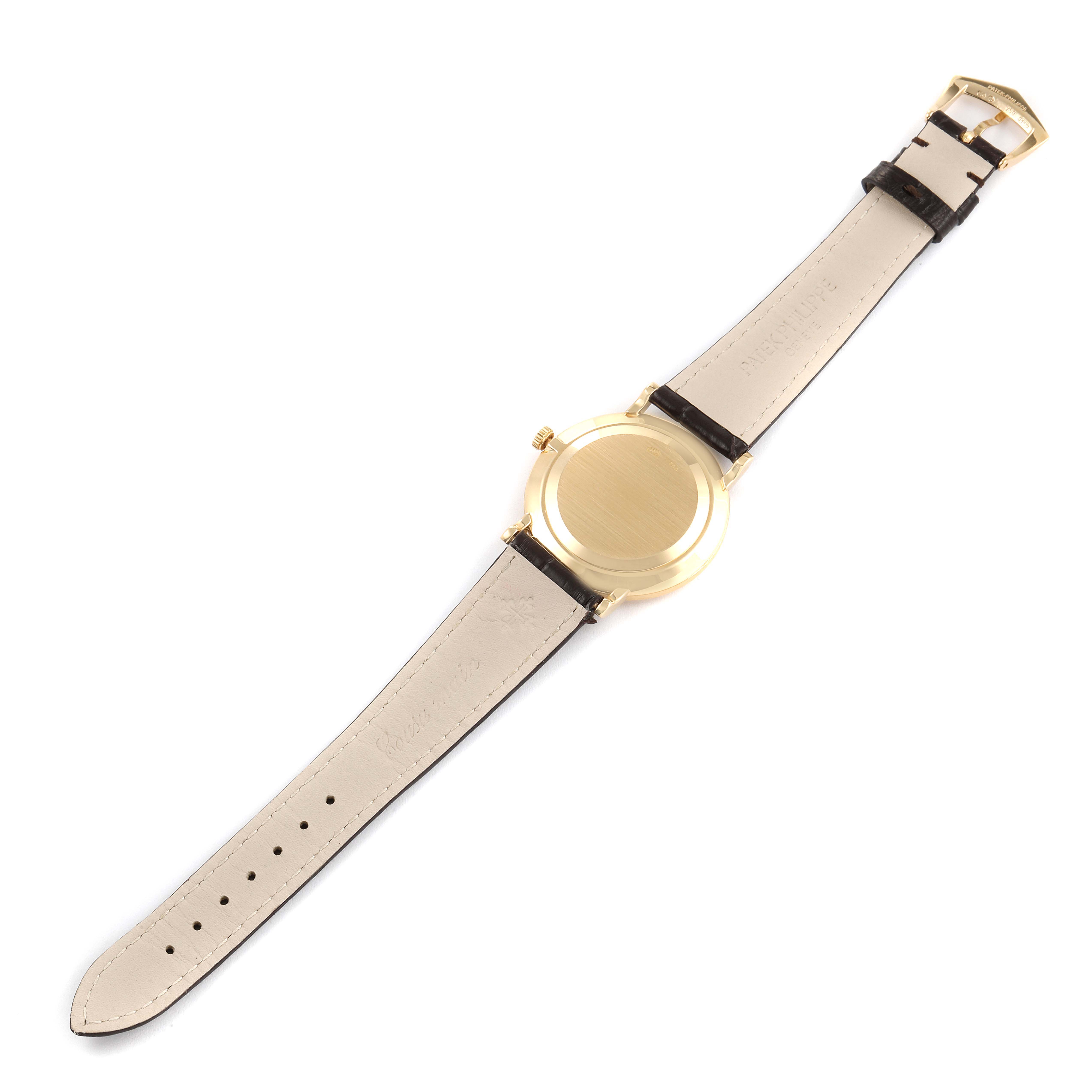 The image shows the backside of a Patek Philippe Calatrava 3919J Men's Yellow Gold White Dial 3919J Men's Yellow Gold White Dial watch laid flat, highlighting the leather strap and metal casing.
