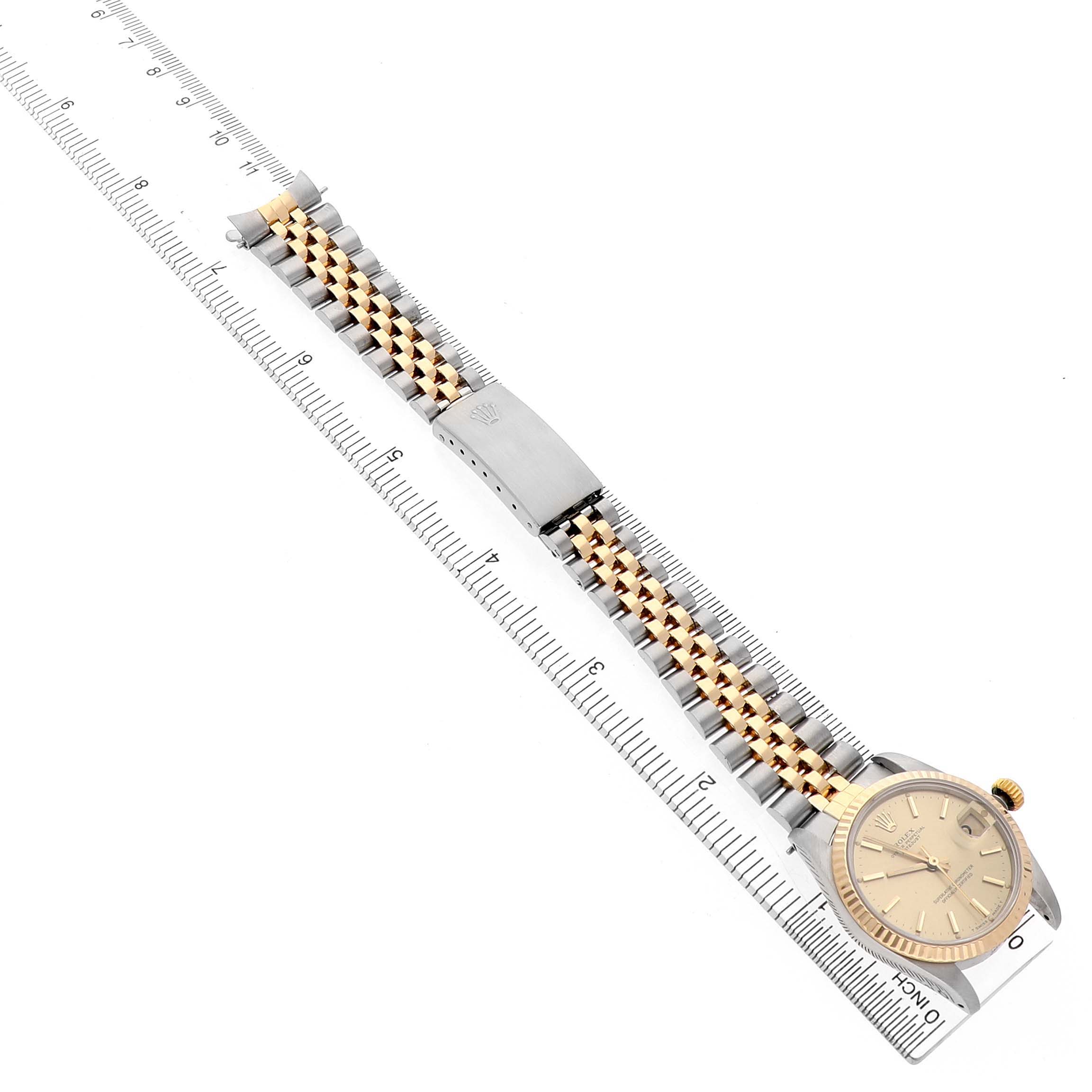 The Rolex Mid-Size 68273 Women's Steel and Gold (two tone) Champagne Dial watch is angled showing the face, bezel, crown, and the full two-tone bracelet alongside a ruler.